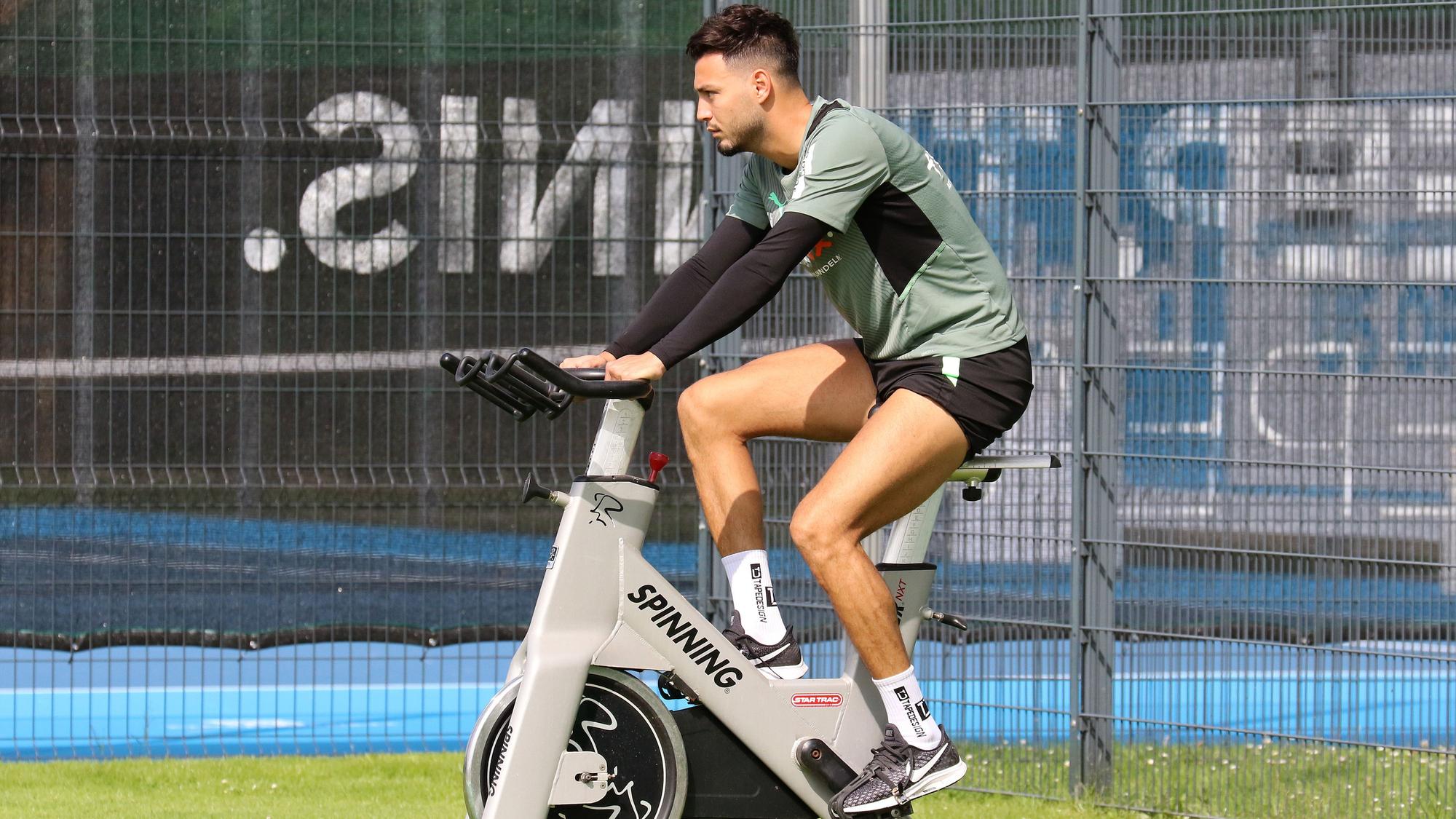 Ramy Bensebaini von Borussia Mönchengladbach sitzt am 18. Juli 2021 auf einem Spinning-Rad während des Trainingslagers in Harsewinkel. Bensebaini schaut nach vorne und radelt.