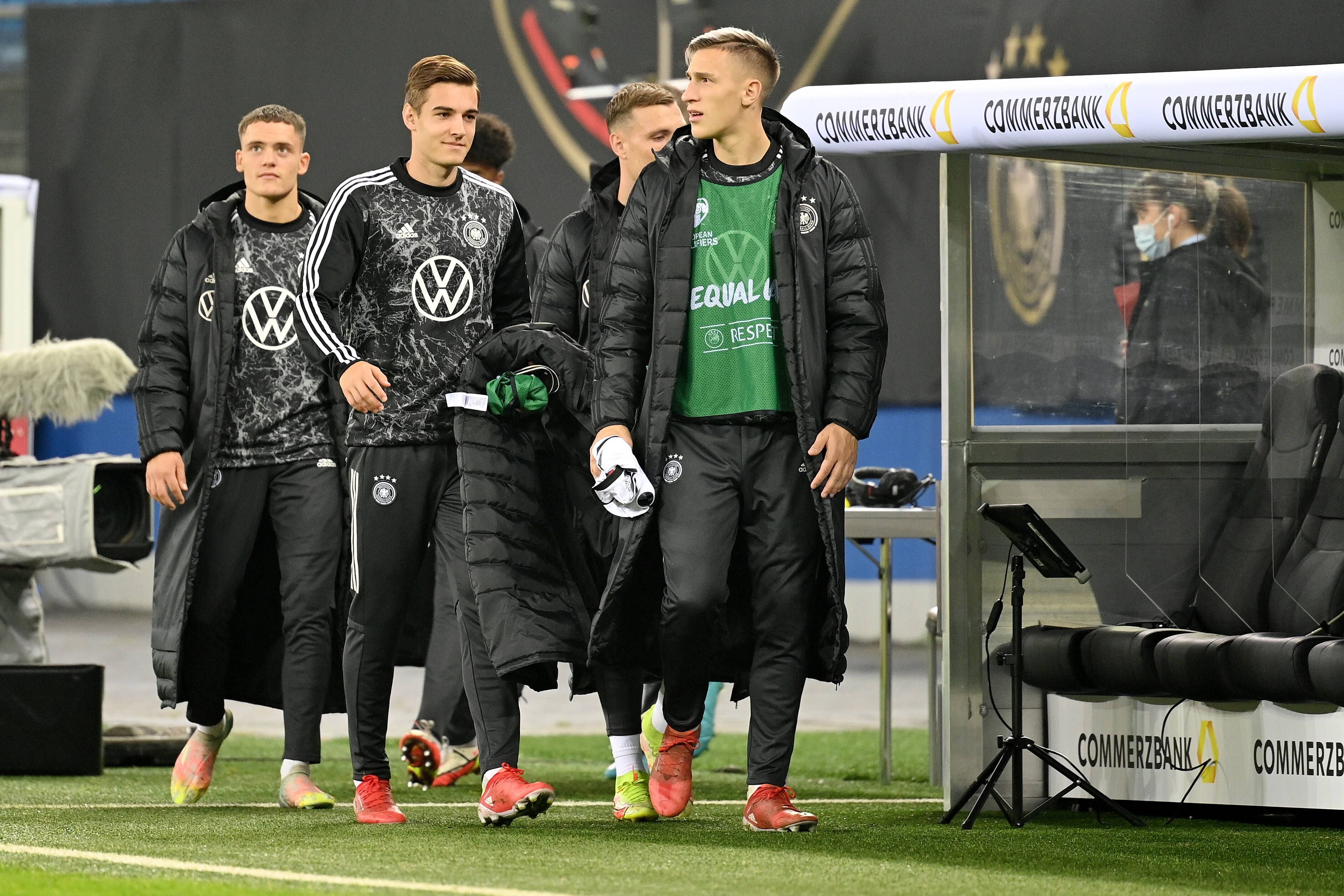 Die Nationalspieler Florian, Florian Neuhaus und Nico Schlotterbeck (v.l.n.r.) schreiten am 8. Oktober 2021 in Hamburg zur Reservebank der DFB-Elf. Neuhaus hält seinen Mantel in der Hand.