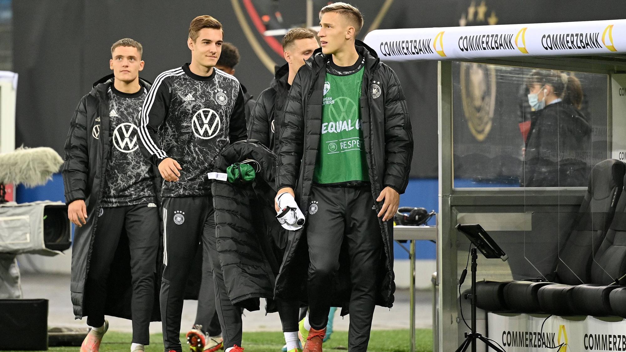 Die Nationalspieler Florian, Florian Neuhaus und Nico Schlotterbeck (v.l.n.r.) schreiten am 8. Oktober 2021 in Hamburg zur Reservebank der DFB-Elf. Neuhaus hält seinen Mantel in der Hand.