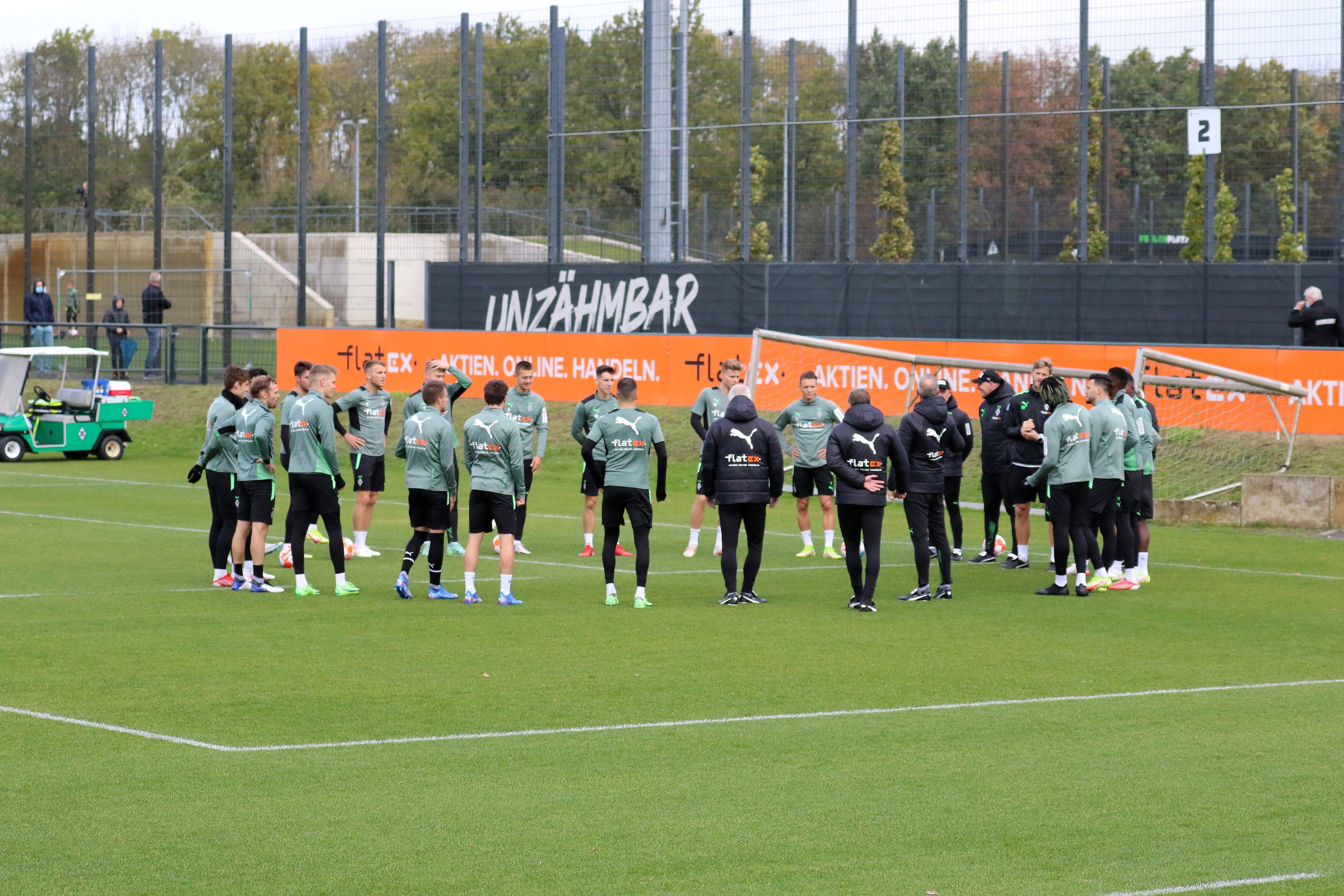 Die Spieler von Borussia Mönchengladbach stehen vor einer Trainingseinheit am 20. Oktober 2021 versammelt auf dem Platz im Borussia-Park, werden dabei von einigen Fans beobachtet.