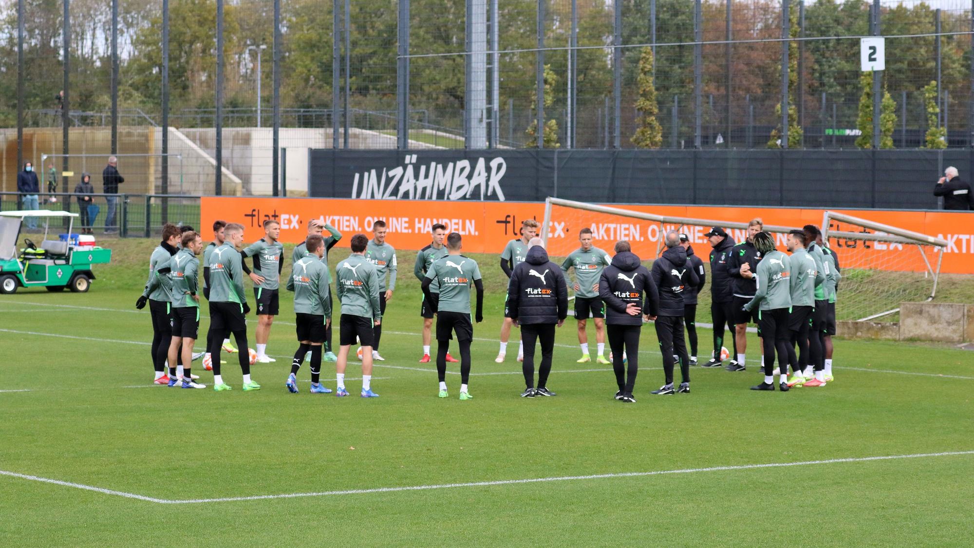 Die Spieler von Borussia Mönchengladbach stehen vor einer Trainingseinheit am 20. Oktober 2021 versammelt auf dem Platz im Borussia-Park, werden dabei von einigen Fans beobachtet.