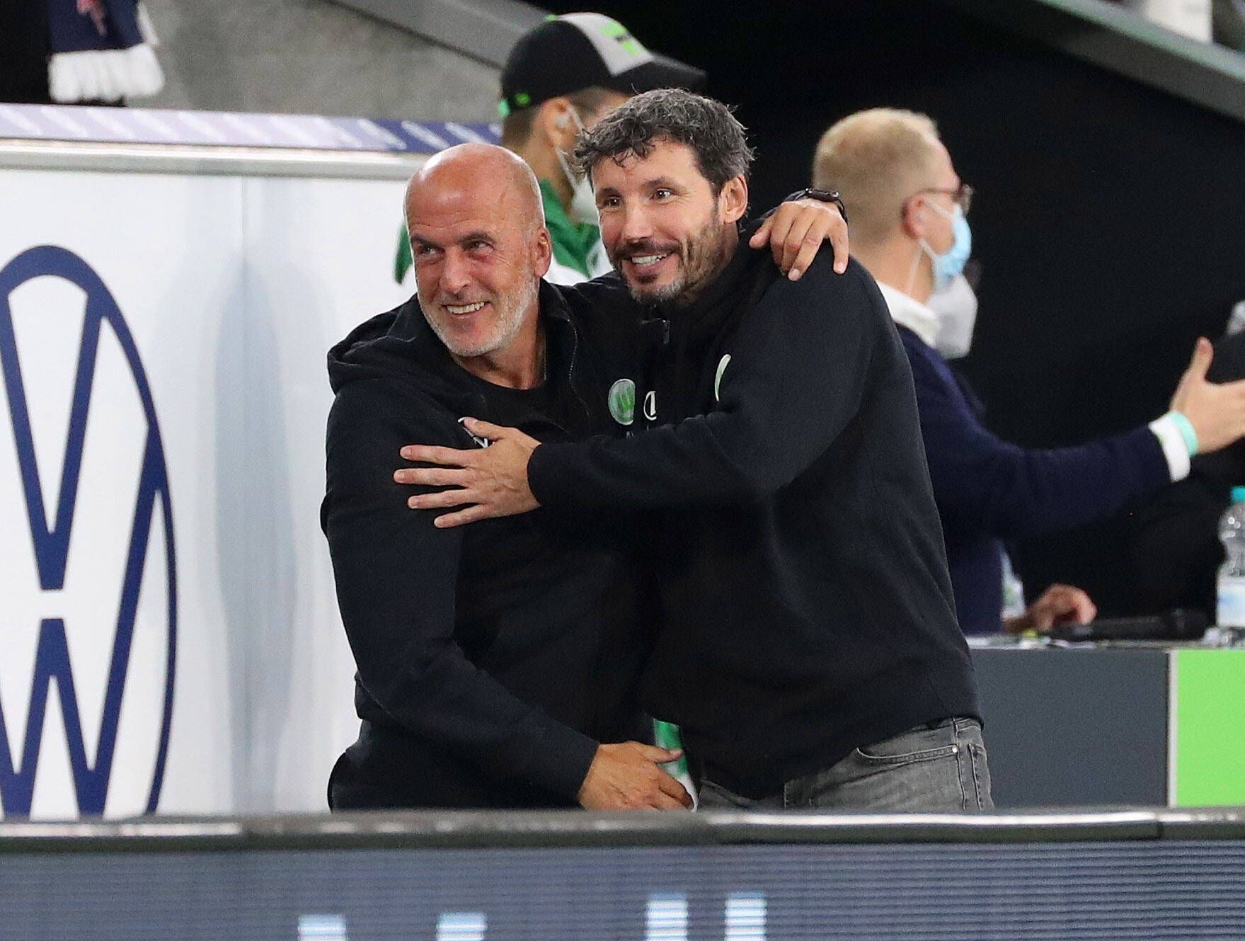 Mark van Bommel (r.) ist am Sonntag (24. Oktober 2021) als Cheftrainer bei Bundesligist VfL Wolfsburg entlassen worden. Muss nun auch sein Assistent Michael Frontzeck, ehemaliger Gladbach-Coach, um seinen Job bangen? Frontzeck und van Bommel umarmen sich. Dieses Foto stammt vom 29. August 2021.