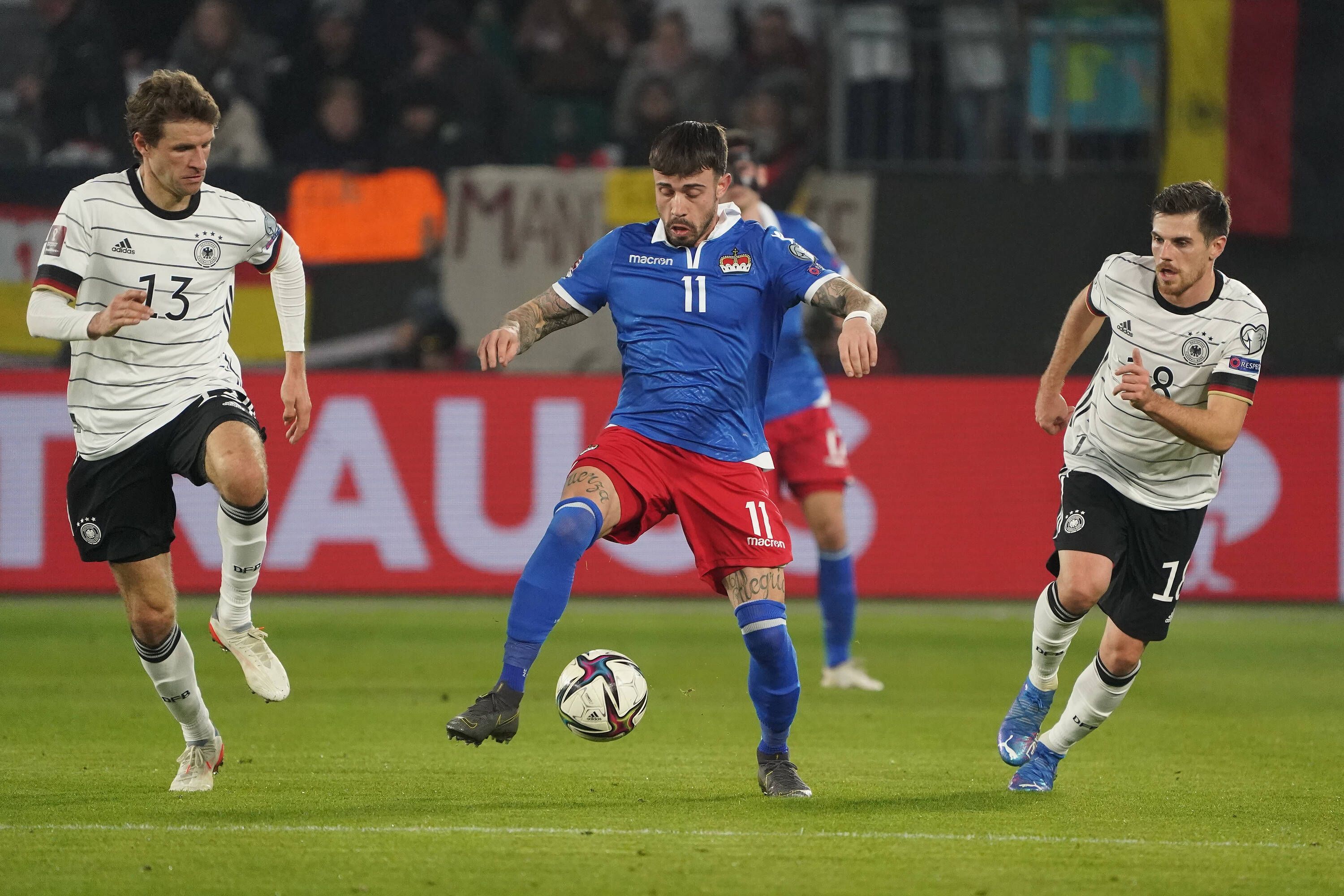 Die deutschen Nationalspieler Thomas Müller (l.) und Jonas Hofmann (r.) im Duell mit Liechtensteins Dennis Salanovic (M.) am 11. November 2021 in der Wolfsburger Arena. Salanovic führt den Ball am rechten Fuß.