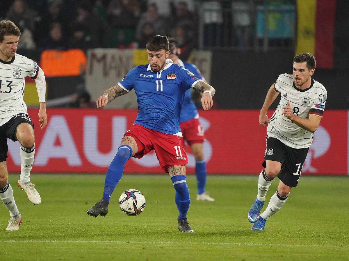Die deutschen Nationalspieler Thomas Müller (l.) und Jonas Hofmann (r.) im Duell mit Liechtensteins Dennis Salanovic (M.) am 11. November 2021 in der Wolfsburger Arena. Salanovic führt den Ball am rechten Fuß.