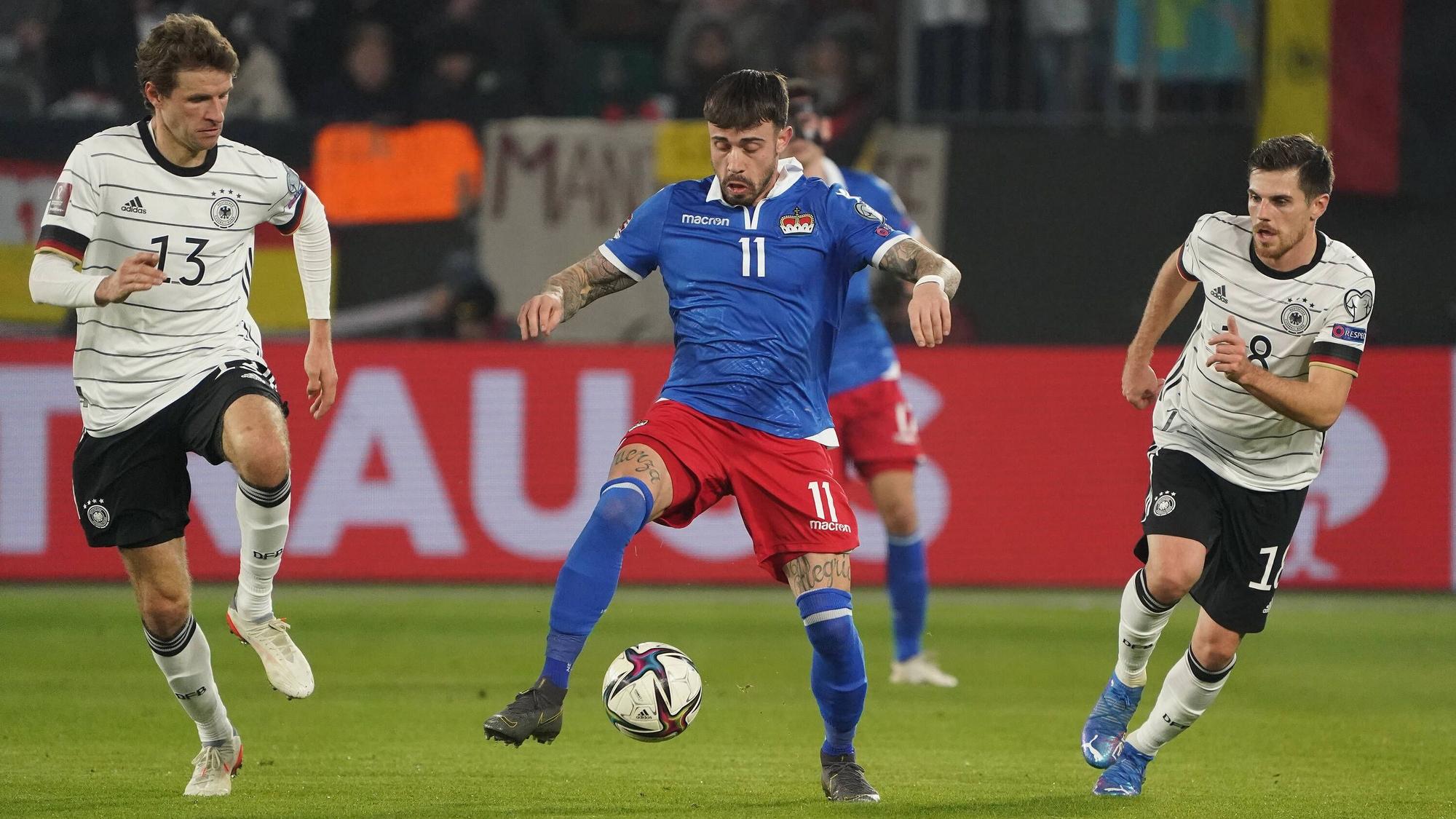 Die deutschen Nationalspieler Thomas Müller (l.) und Jonas Hofmann (r.) im Duell mit Liechtensteins Dennis Salanovic (M.) am 11. November 2021 in der Wolfsburger Arena. Salanovic führt den Ball am rechten Fuß.