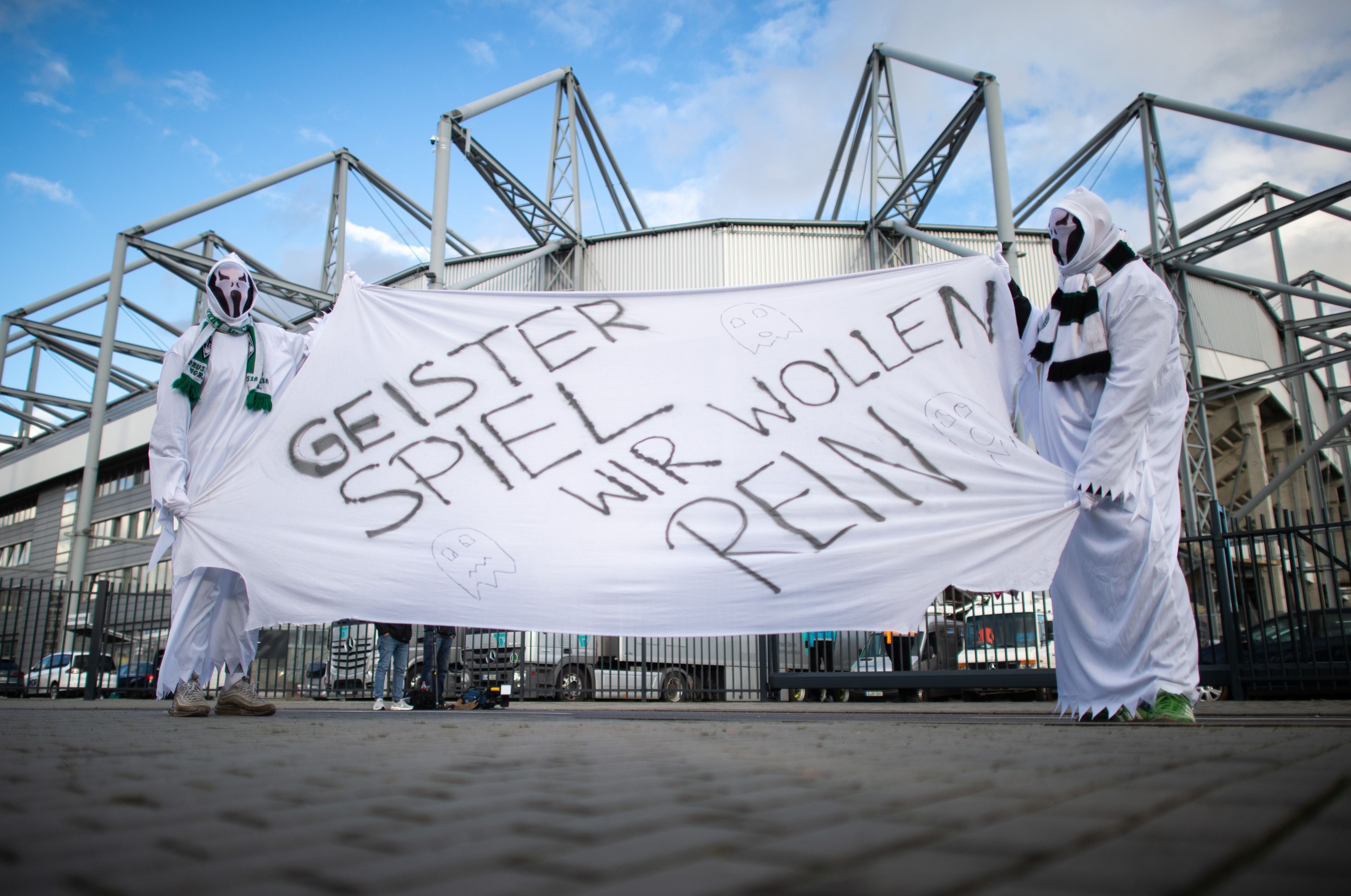 Zwei als Geist verkleidete Gladbach-Fans stehen vor dem Derby gegen den 1. FC Köln am 11. März 2020 vor den Toren des Borussia-Parks. Sie zeigen ein Banner mit der Aufschrift „Geisterspiel, wir wollen rein“.