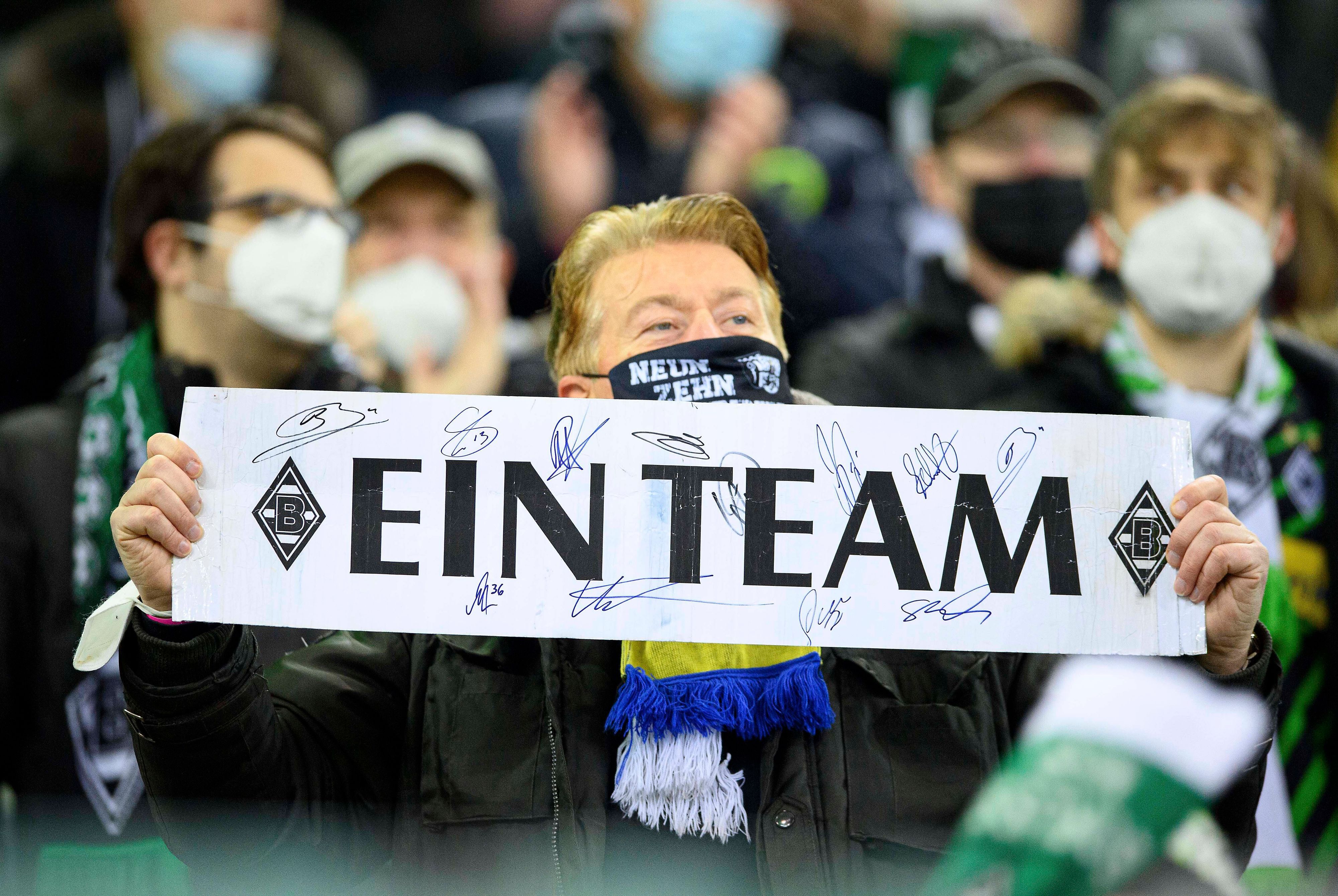 Ein Fan von Fußball-Bundesligist Borussia Mönchengladbach zeigt ein Plakat mit der Aufschrift „Ein Team“. Dieses Foto aus dem Borussia-Park ist am 5. Dezember 2021 entstanden.