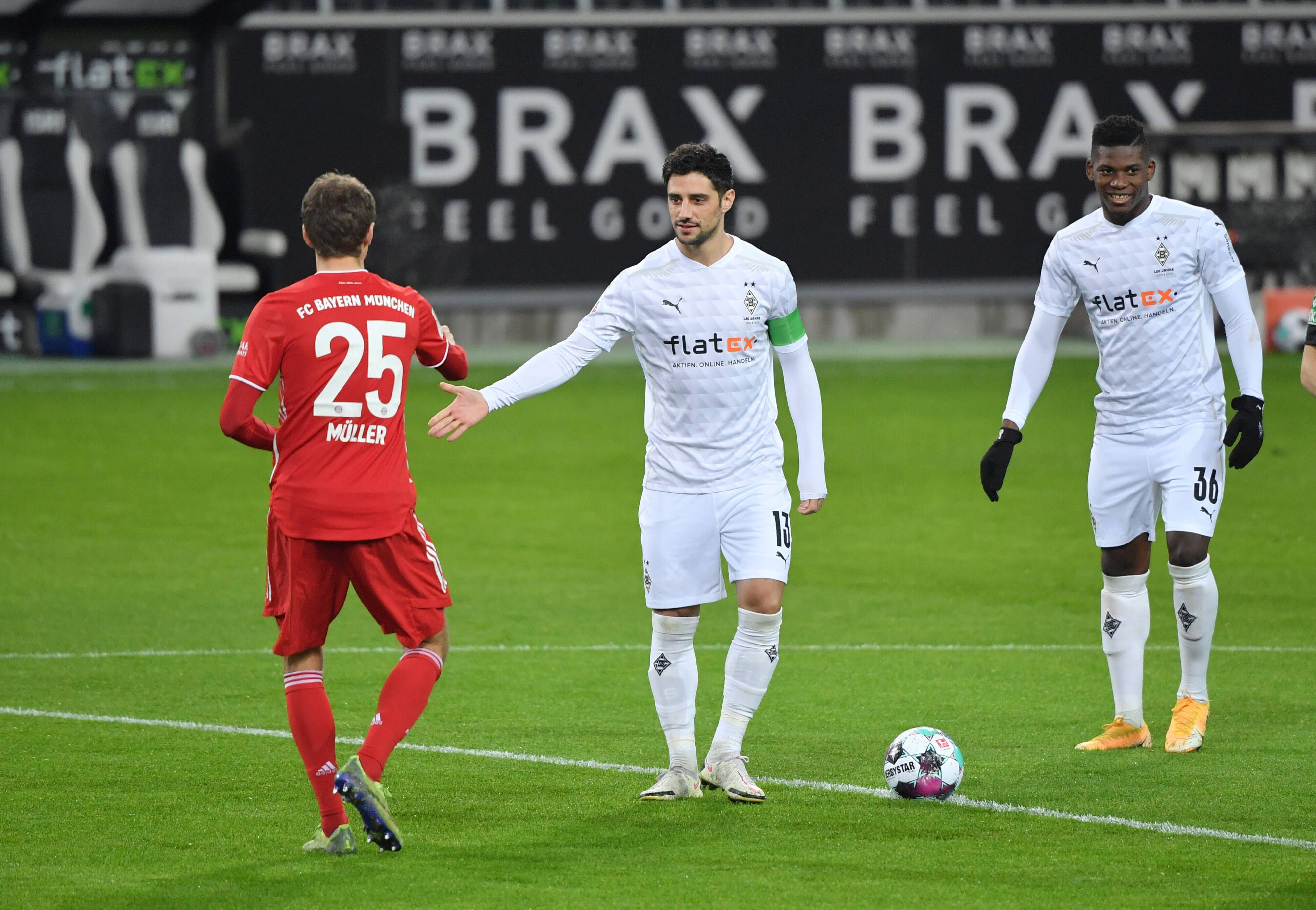 Gladbach-Kapitän Lars Stindl klatscht sich am 8. Januar 2021 am Mittelkreis mit Bayern-München-Star Thomas Müller (l.) ab, derweil schaut Fohlen-Stürmer Breel Embolo (r.) zu.