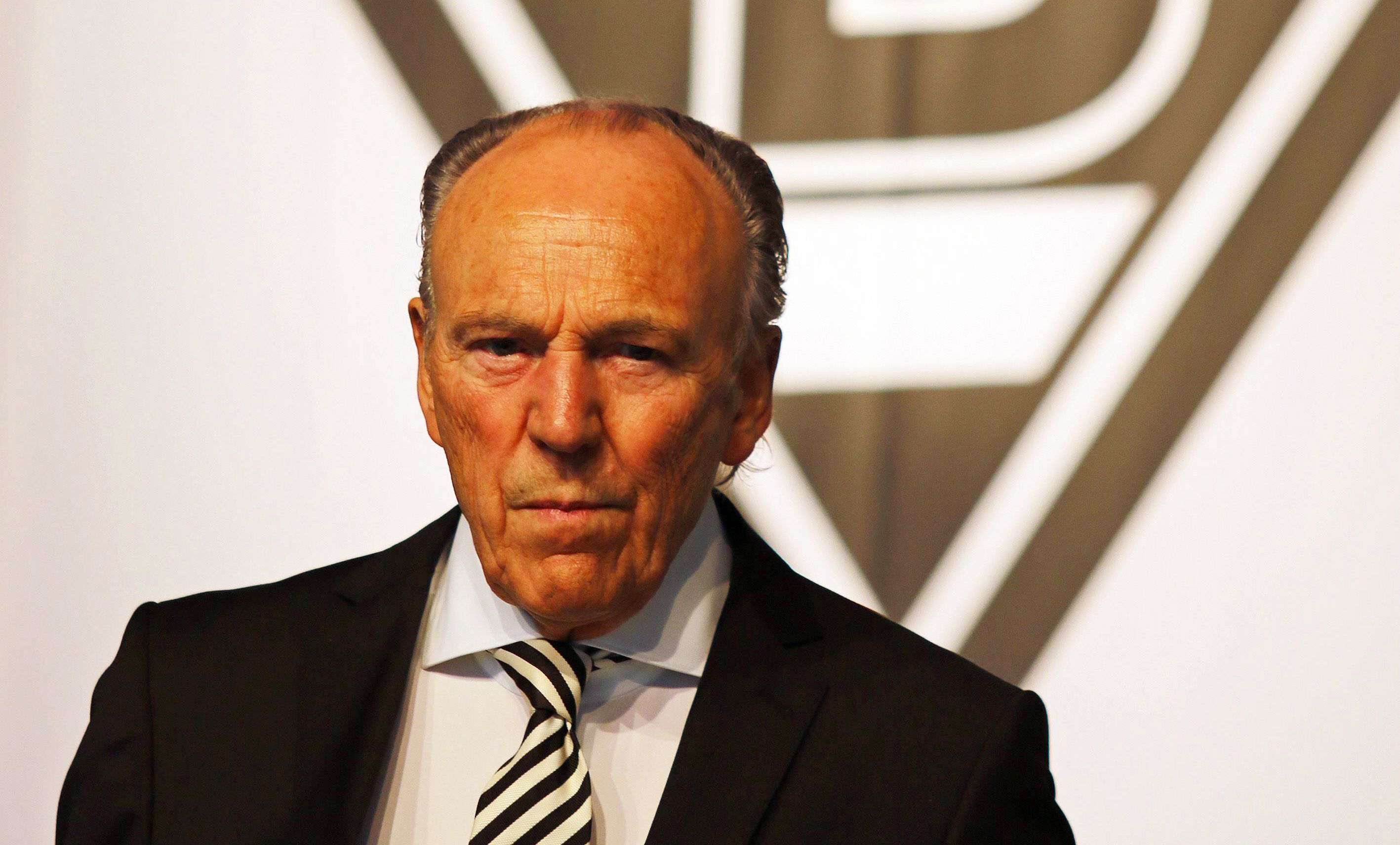Gladbach-Präsident Rolf Königs steht vor einer Borussia-Fahne und blickt mit ernster Miene in die Kamera.