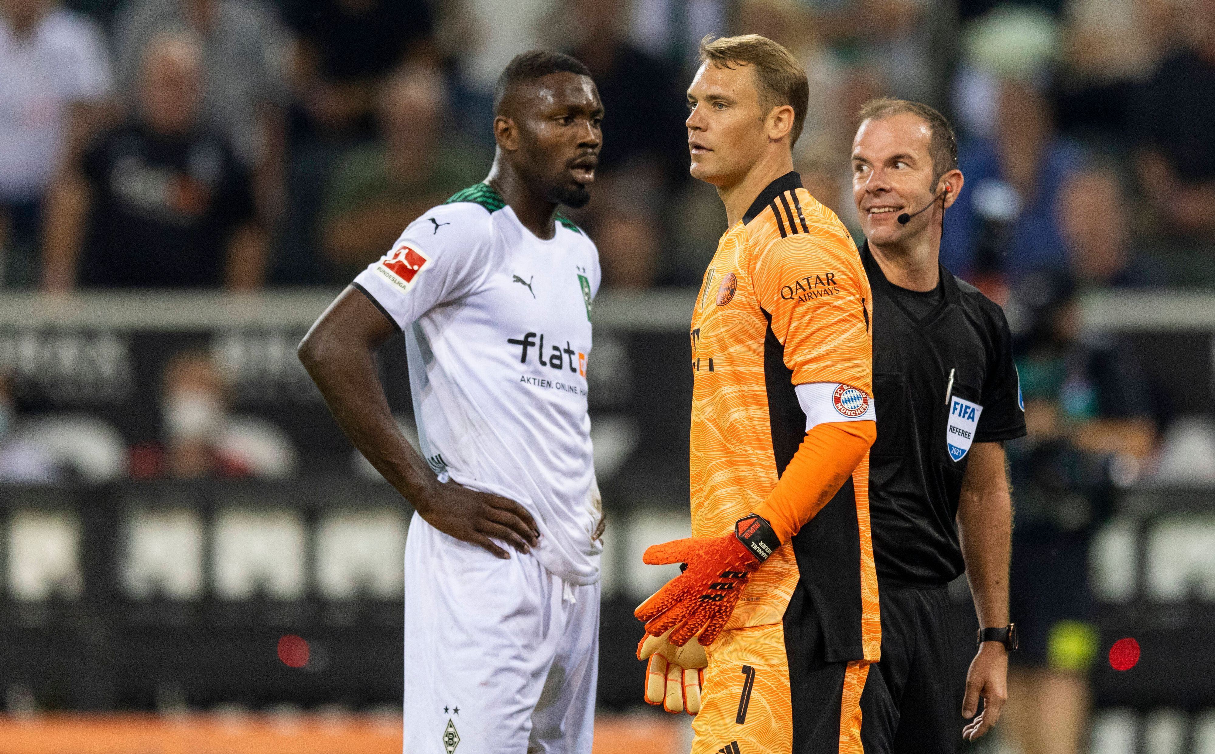 Gladbach-Stürmer Marcus Thuram (l.) mit Bayern-München-Torhüter Manuel Neuer (M.) und Schiedsrichter Marco Fritz (r.) beim Bundesliga-Hinspiel am 13. August 2021. Marco Fritz lächelt.