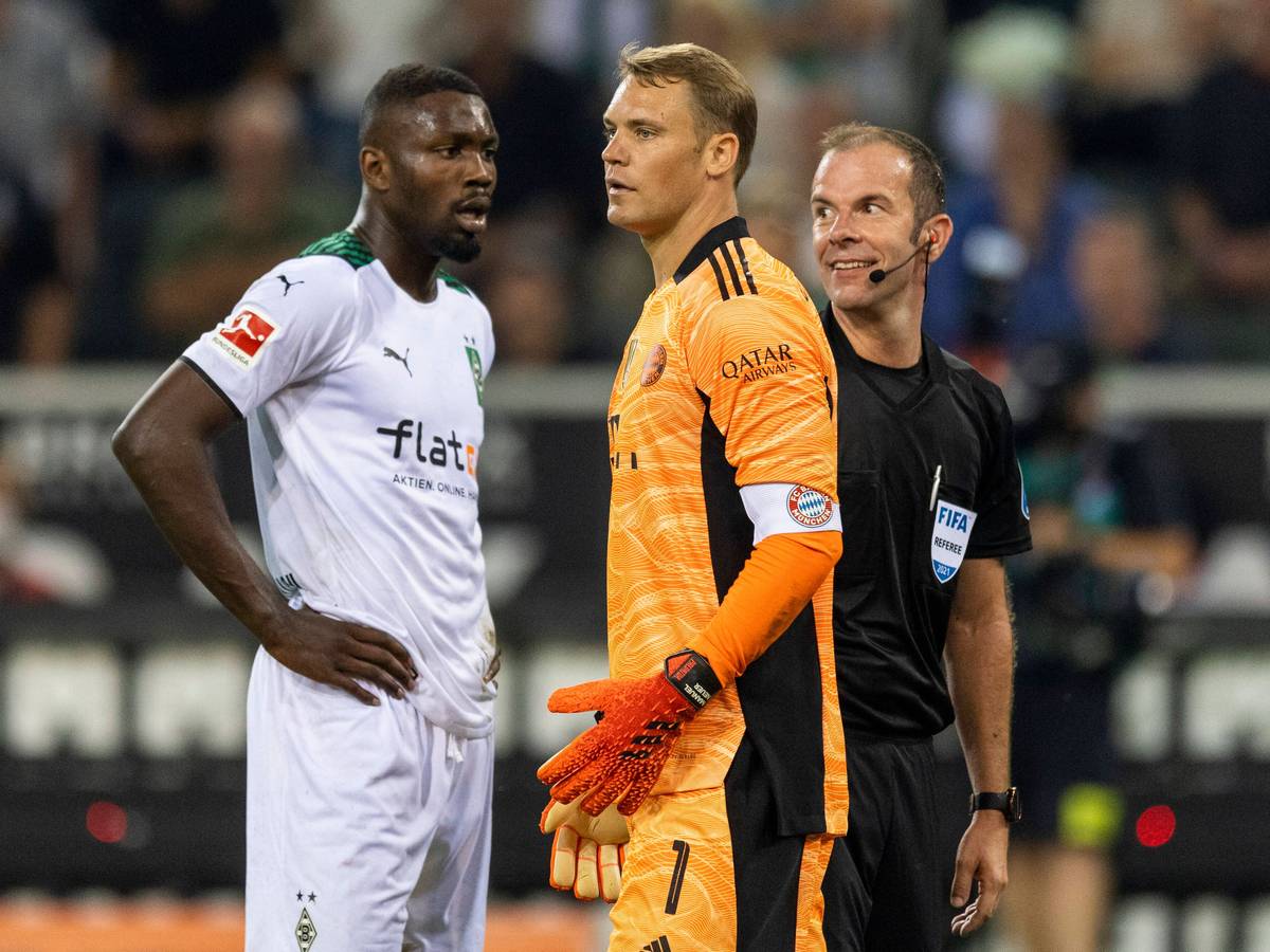 Gladbach-Stürmer Marcus Thuram (l.) mit Bayern-München-Torhüter Manuel Neuer (M.) und Schiedsrichter Marco Fritz (r.) beim Bundesliga-Hinspiel am 13. August 2021. Marco Fritz lächelt.