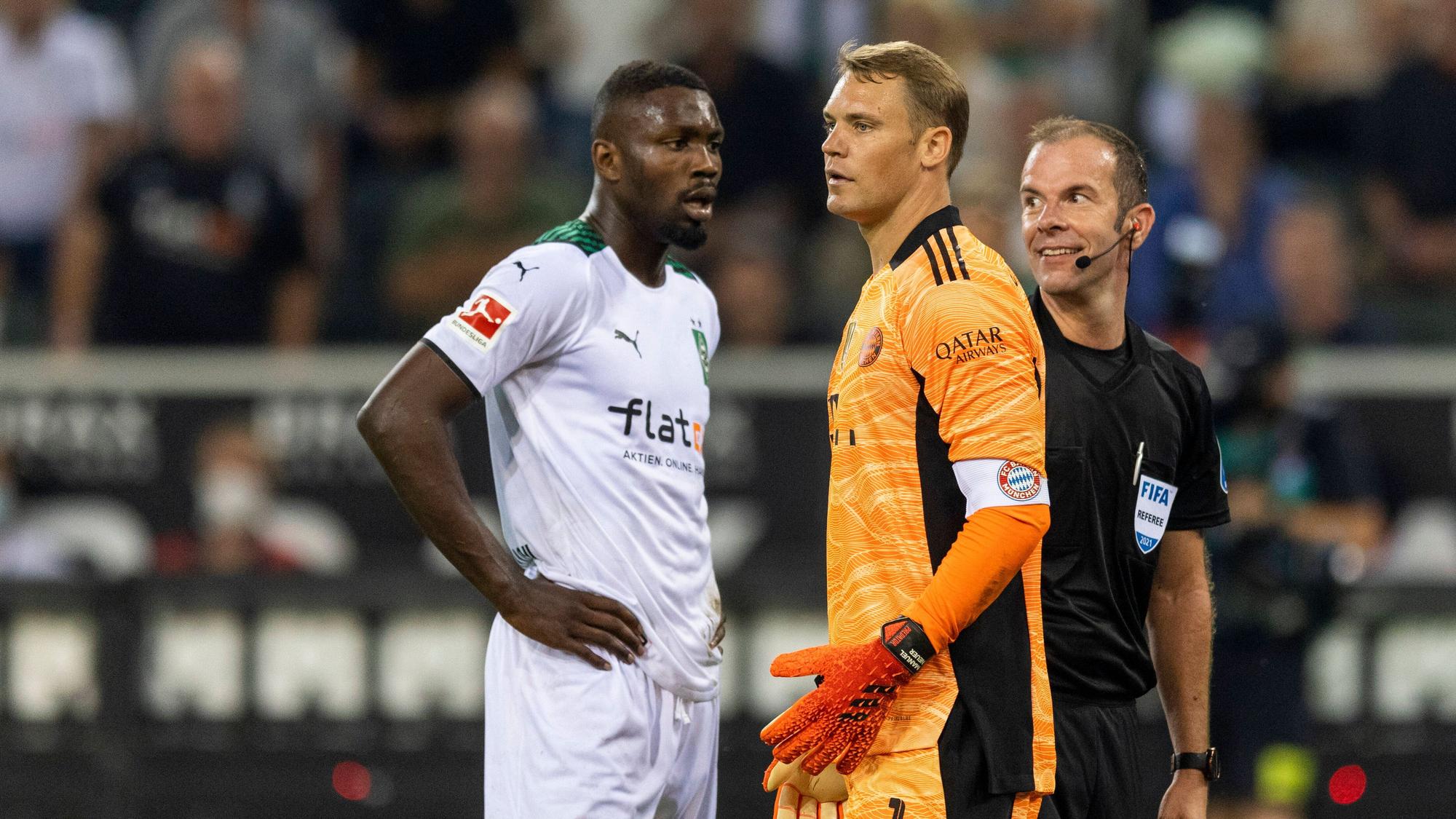 Gladbach-Stürmer Marcus Thuram (l.) mit Bayern-München-Torhüter Manuel Neuer (M.) und Schiedsrichter Marco Fritz (r.) beim Bundesliga-Hinspiel am 13. August 2021. Marco Fritz lächelt.