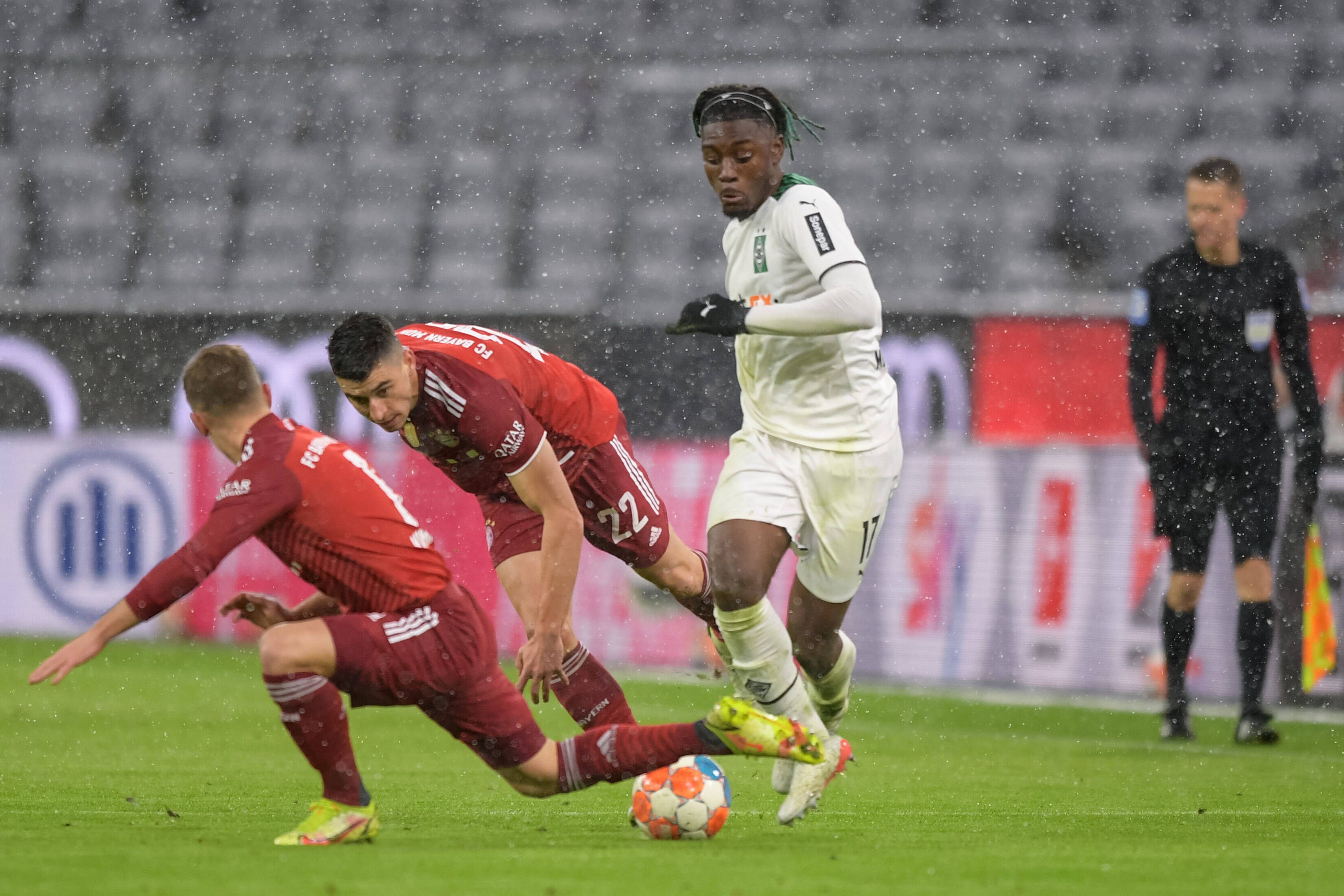 Manu Kone (r.), Mittelfeldakteur von Borussia Mönchengladbach, setzt sich im Bundesliga-Duell bei Bayern München (7. Januar 2022) gegen zwei Gegenspieler durch. Kone dribbelt mit dem Ball.