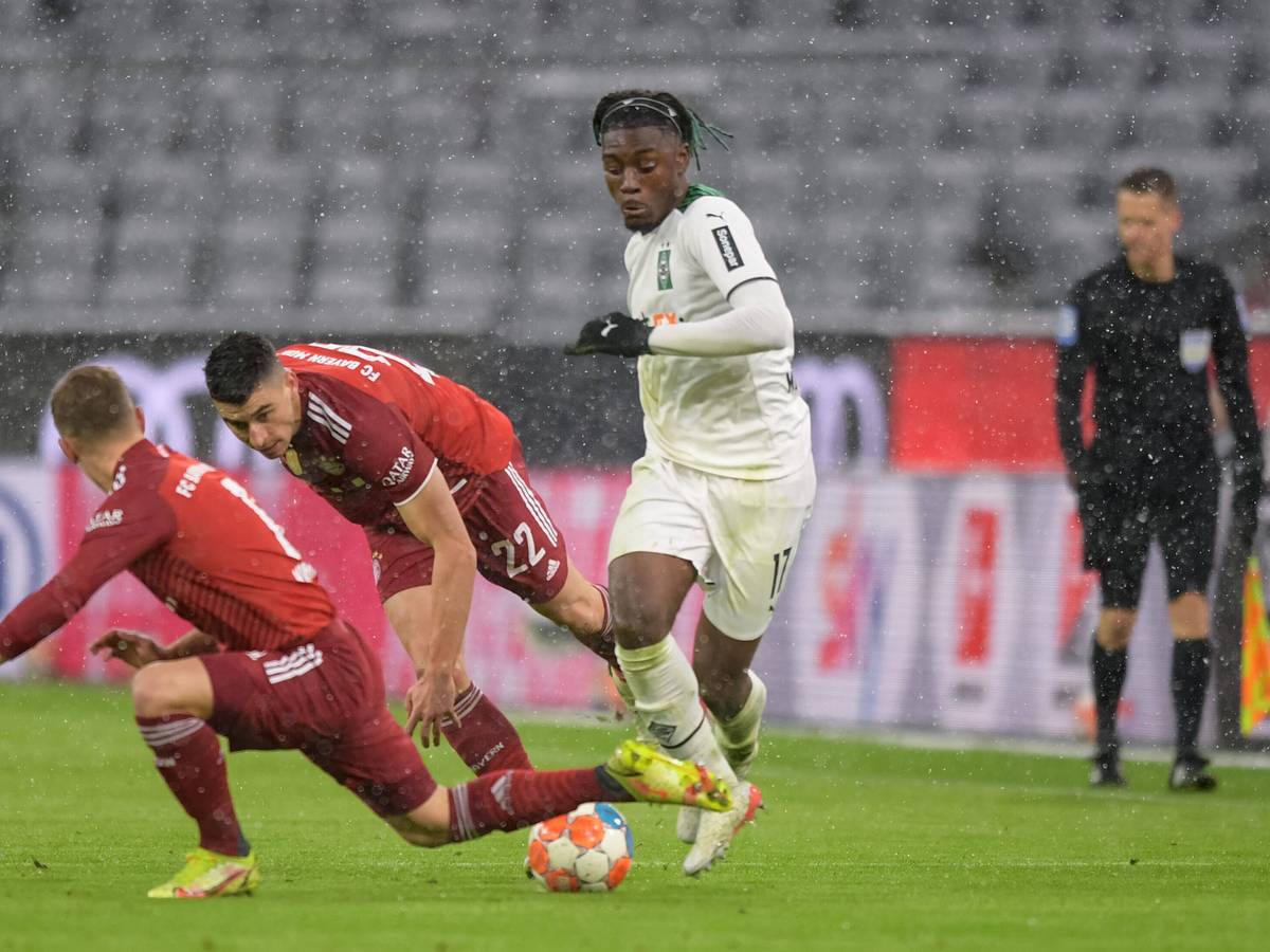 Manu Kone (r.), Mittelfeldakteur von Borussia Mönchengladbach, setzt sich im Bundesliga-Duell bei Bayern München (7. Januar 2022) gegen zwei Gegenspieler durch. Kone dribbelt mit dem Ball.