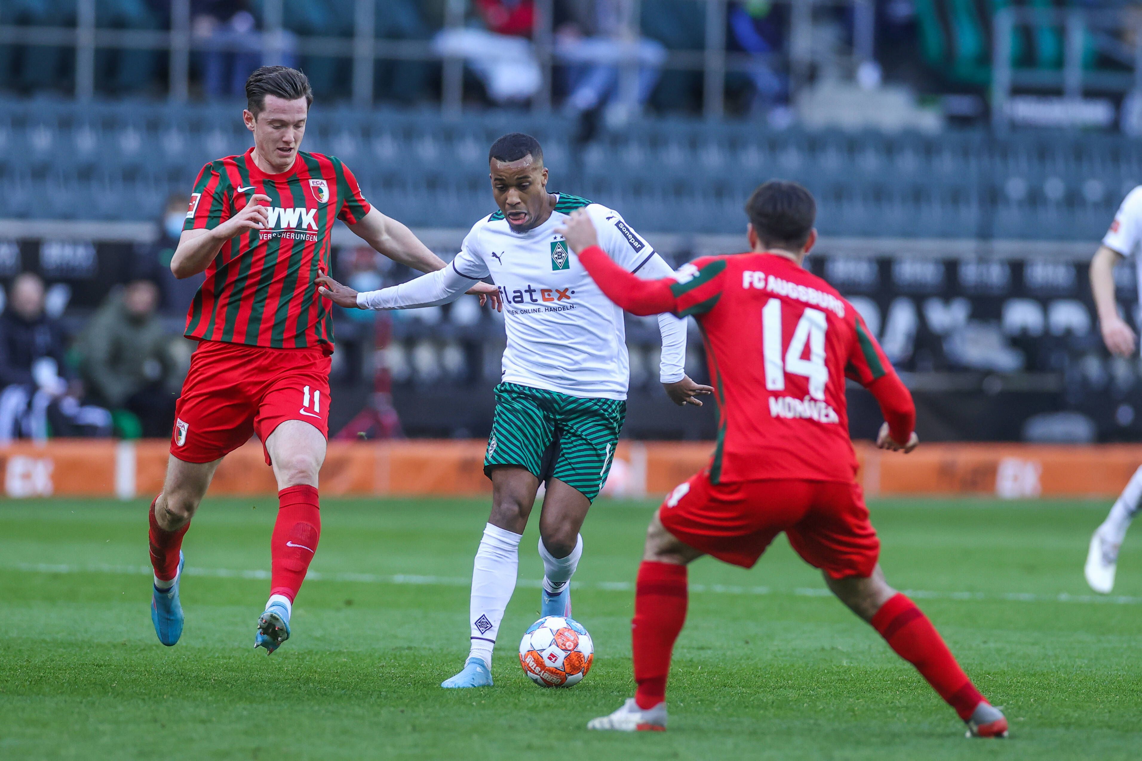 Gladbachs Offensivspieler Alassane Plea (Mitte) im Zweikampf mit Augsburgs Michael Gregoritsch (l.) am 12. Februar 2022 im Borussia-Park.