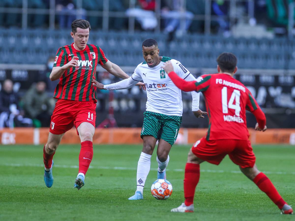 Gladbachs Offensivspieler Alassane Plea (Mitte) im Zweikampf mit Augsburgs Michael Gregoritsch (l.) am 12. Februar 2022 im Borussia-Park.