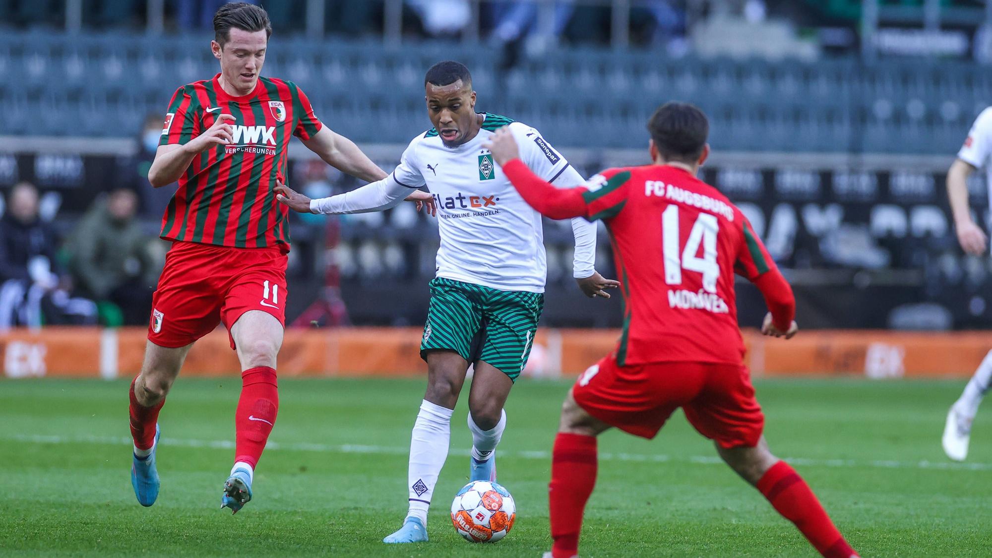 Gladbachs Offensivspieler Alassane Plea (Mitte) im Zweikampf mit Augsburgs Michael Gregoritsch (l.) am 12. Februar 2022 im Borussia-Park.