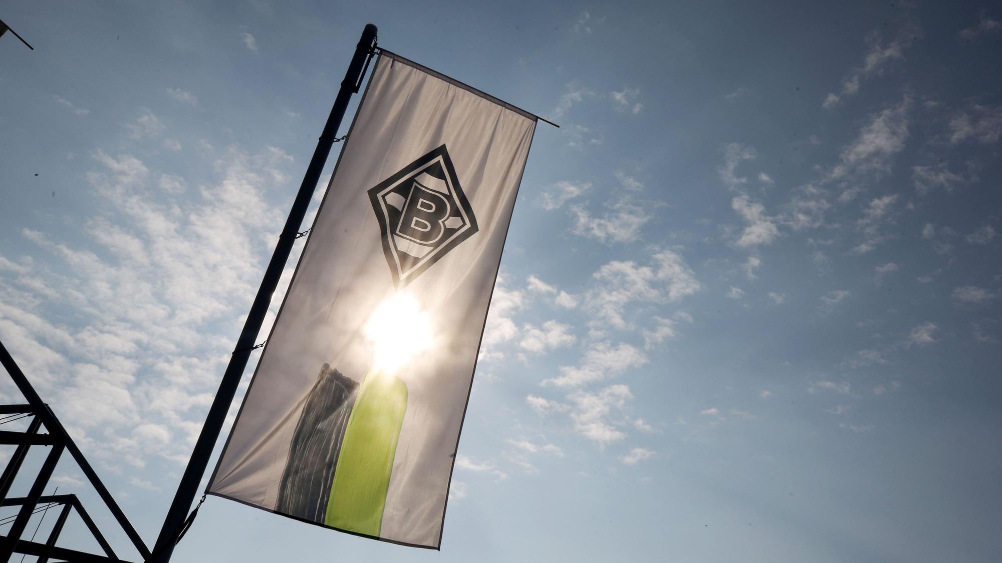 Eine Fahne mit dem Logo von Borussia Mönchengladbach weht am Borussia-Park. Auf dem Symbolfoto scheint die Sonne, sie wird von der Fahne allerdings verdeckt.