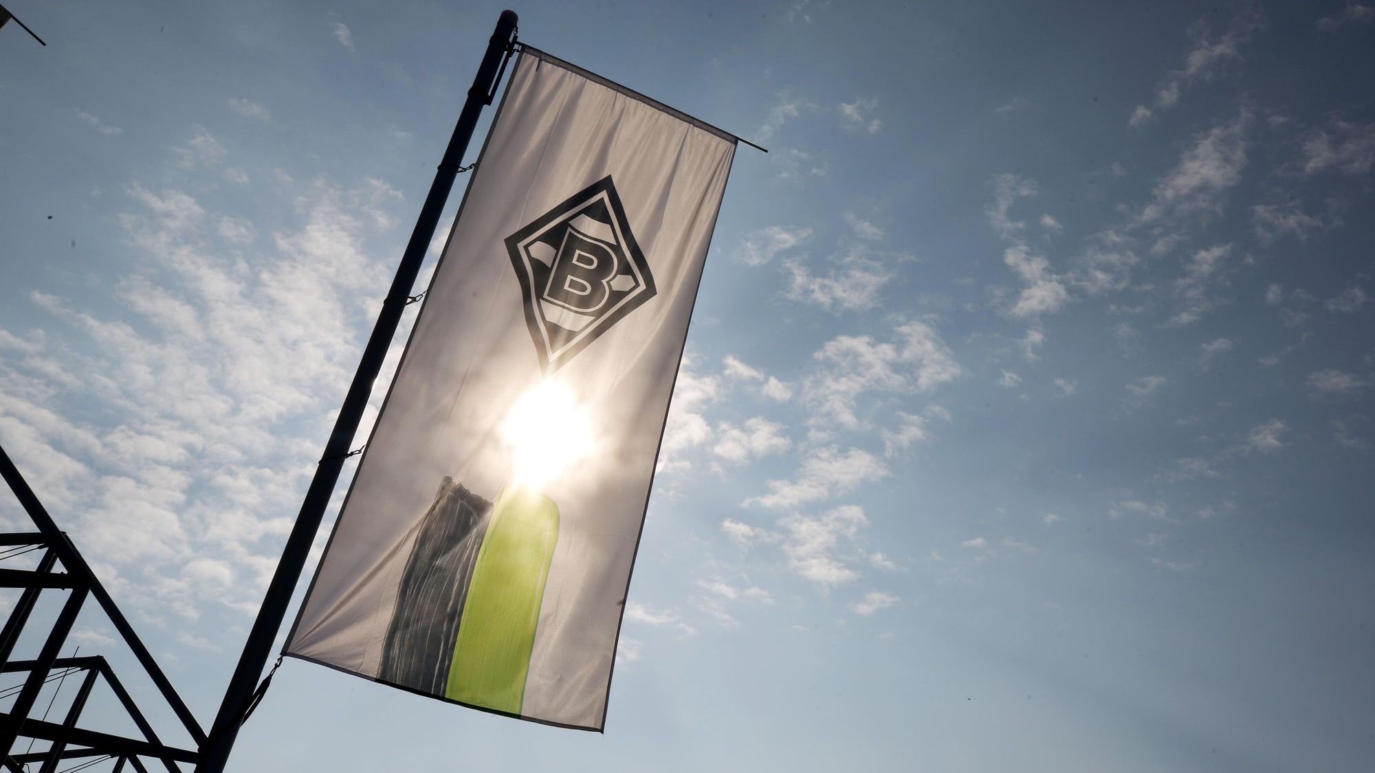 Eine Fahne mit dem Logo von Borussia Mönchengladbach weht am Borussia-Park. Im Hintergrund scheint die Sonne.