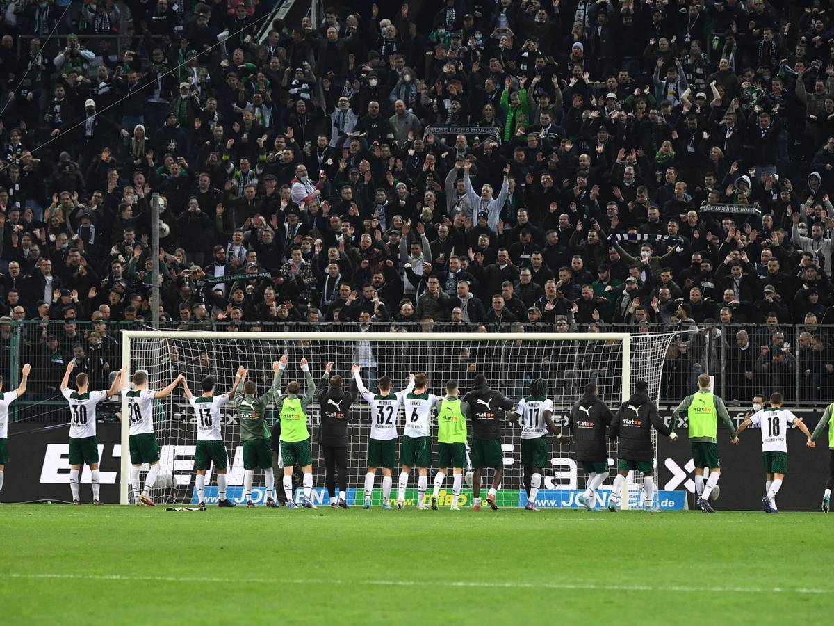 Die Spieler von Borussia Mönchengladbach feiern am Samstag (12. März 2022) gemeinsam mit den Fans den Heimsieg im Abstiegskampf gegen Hertha BSC. Die Gladbach-Spieler bilden eine Kette und heben gemeinsam die Arme.