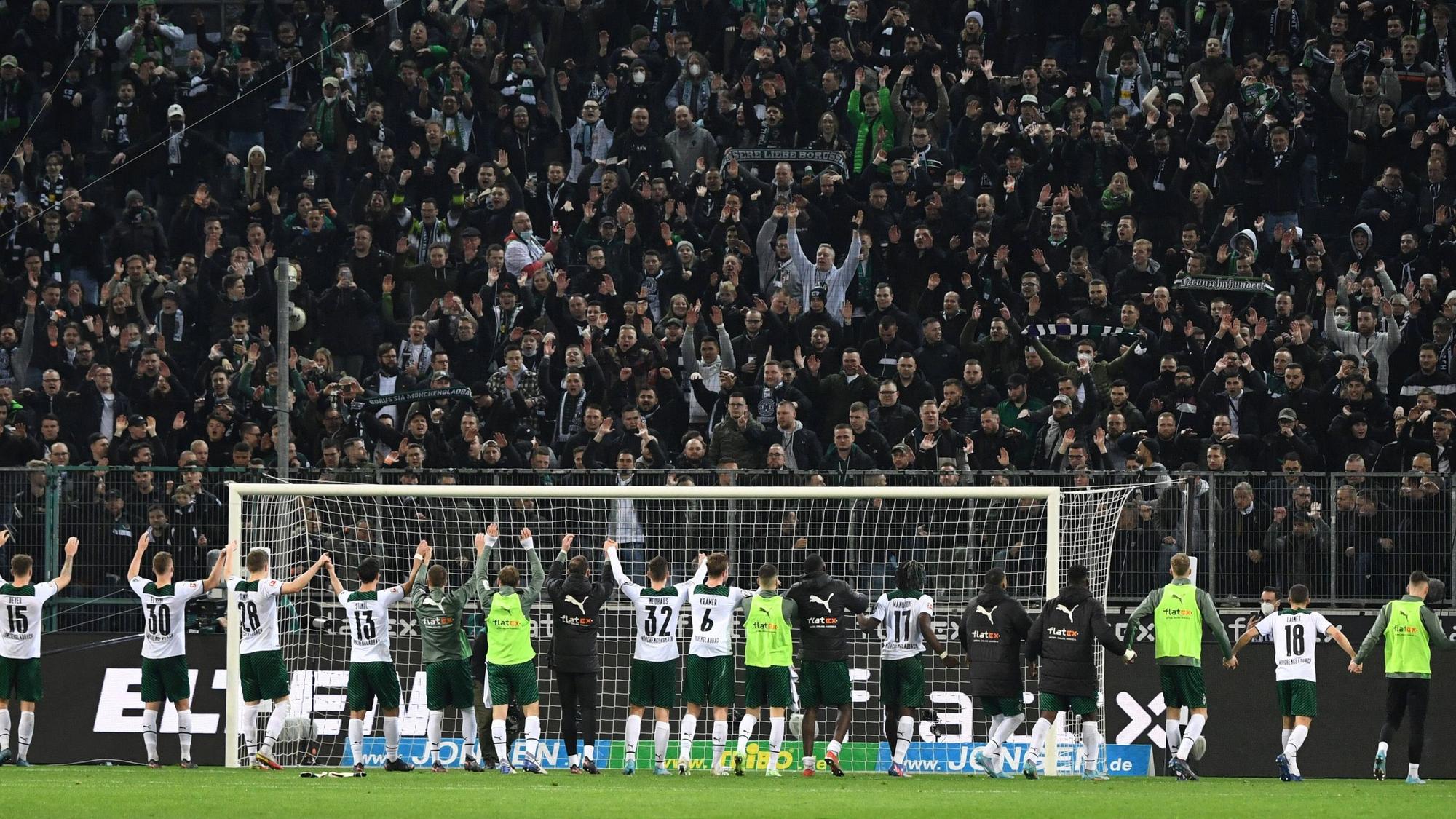 Die Spieler von Borussia Mönchengladbach feiern am Samstag (12. März 2022) gemeinsam mit den Fans den Heimsieg im Abstiegskampf gegen Hertha BSC. Die Gladbach-Spieler bilden eine Kette und heben gemeinsam die Arme.