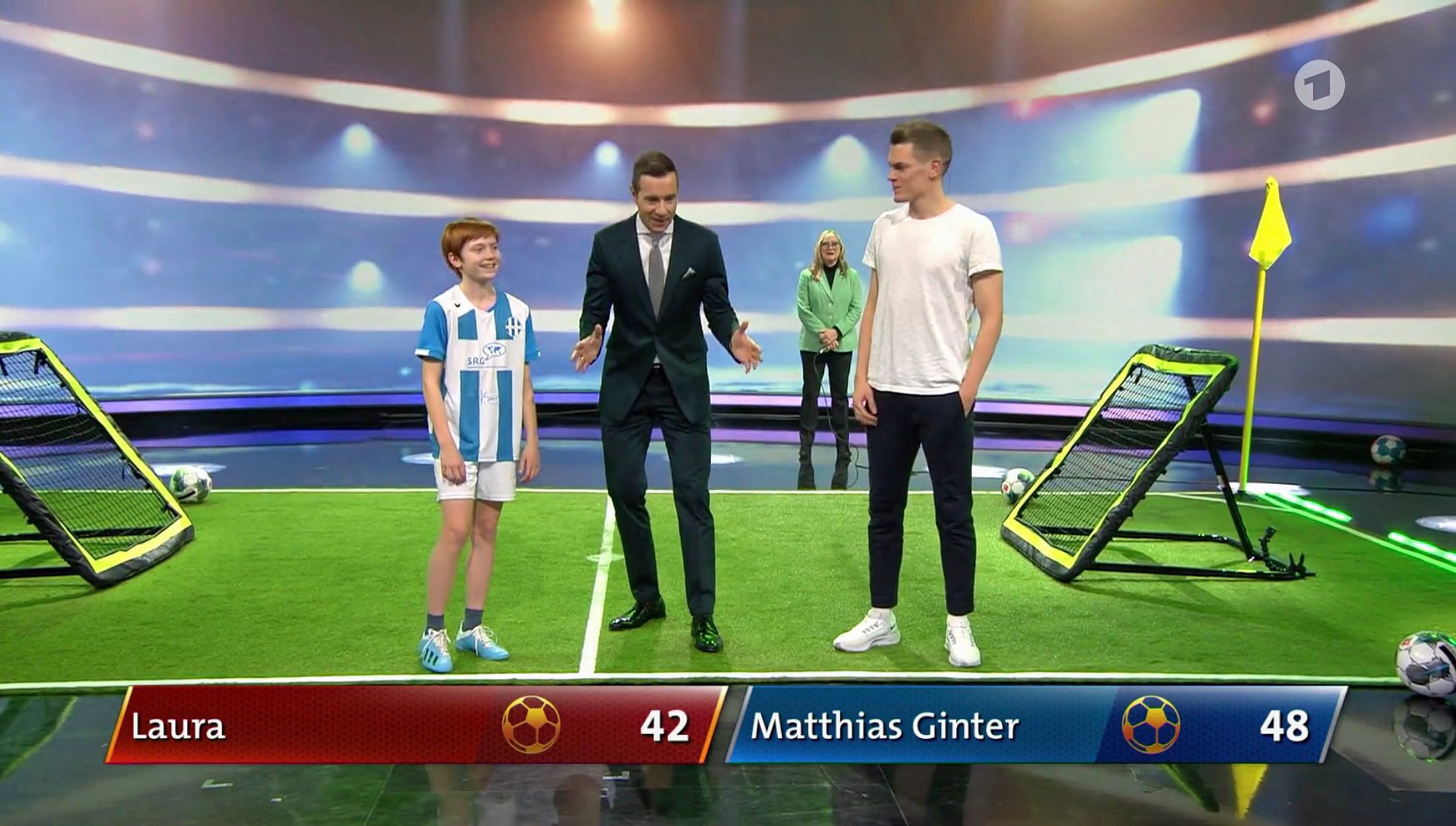 Moderator Kai Pflaume (Mitte) mit Nationalspieler Matthias Ginter (r.) von Borussia Mönchengladbach und der 13-jährigen Laura (l.) in der ARD-Sendung „Klein gegen Groß – Das unglaubliche Duell“ am 12. März 2022. Pflaume macht eine Geste, Ginter und Laura lachen.