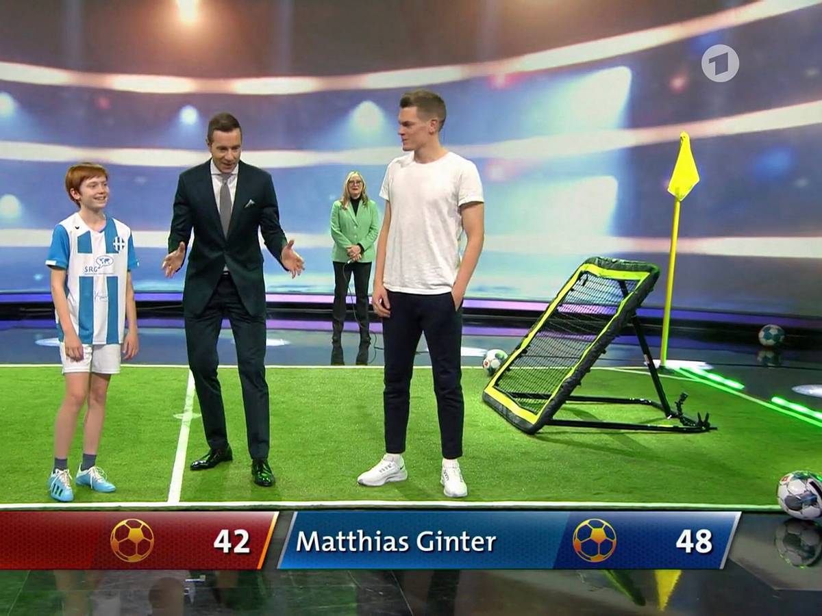 Moderator Kai Pflaume (Mitte) mit Nationalspieler Matthias Ginter (r.) von Borussia Mönchengladbach und der 13-jährigen Laura (l.) in der ARD-Sendung „Klein gegen Groß – Das unglaubliche Duell“ am 12. März 2022. Pflaume macht eine Geste, Ginter und Laura lachen.