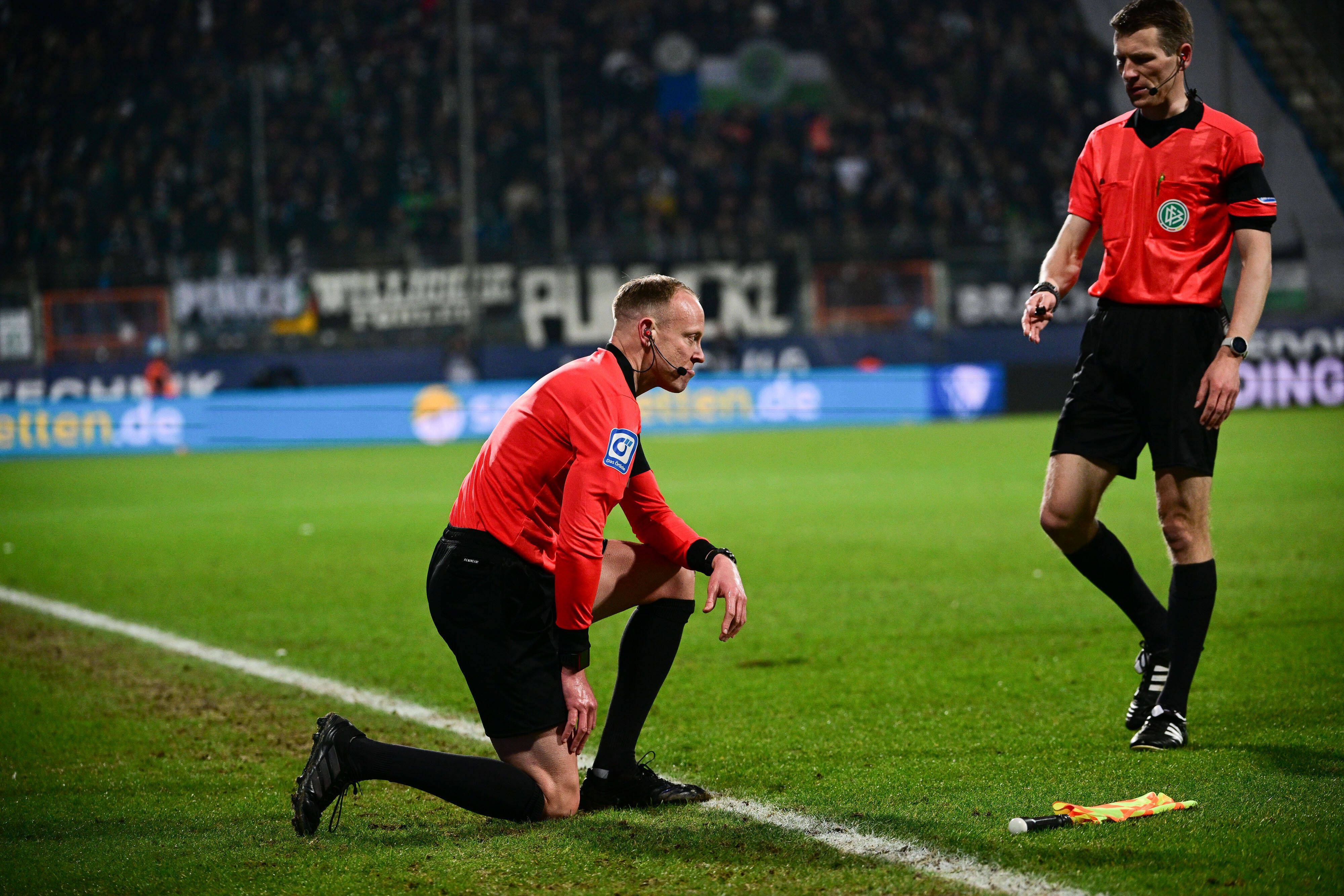 Schiedsrichter-Assistent Christian Gittelmann geht zu Boden, getroffen von einem Bierbecher im Bundesliga-Duell zwischen dem VfL Bochum und Borussia Mönchengladbach am 18, März 2022. Schiedsrichter Cortus kommt zu Hilfe.