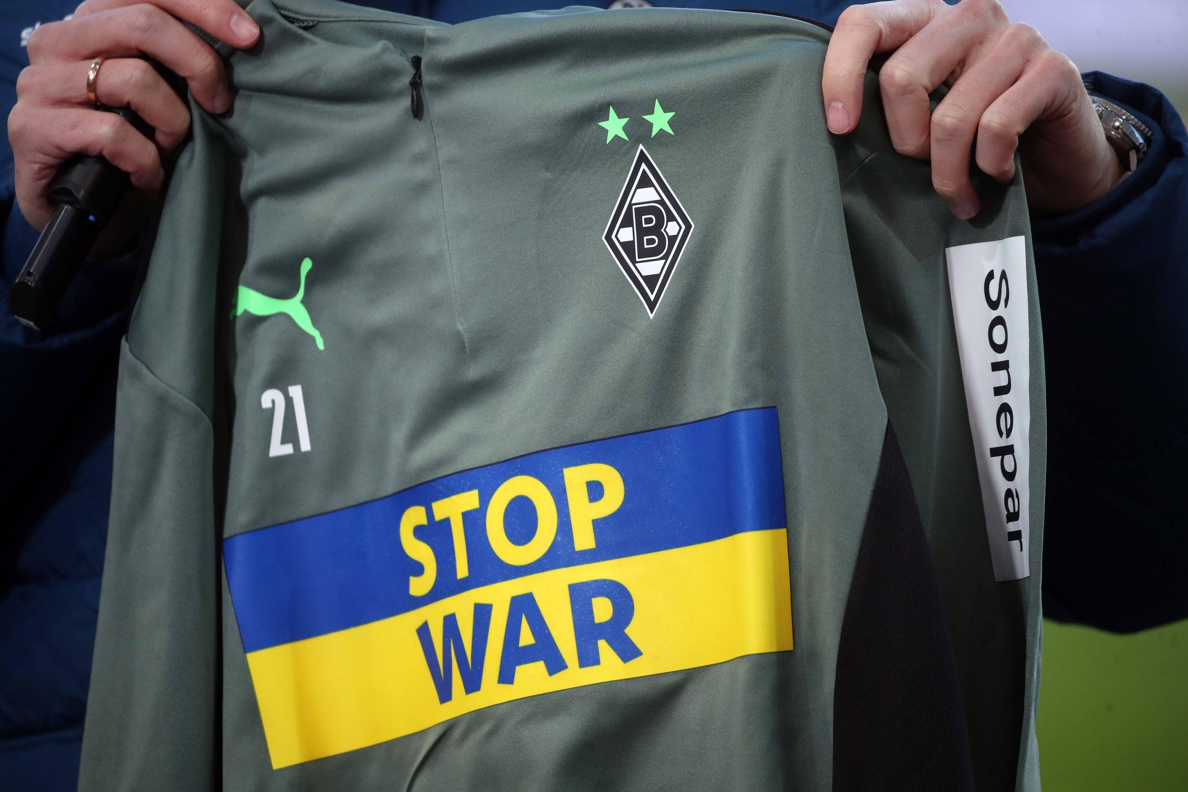 Um dieses schöne Stück geht es. Die Aufwärmshirts von Borussia Mönchengladbach mit der Botschaft „Stop War“ stehen noch zur Auktion. Das Shirt wird in die Kamera präsentiert.
