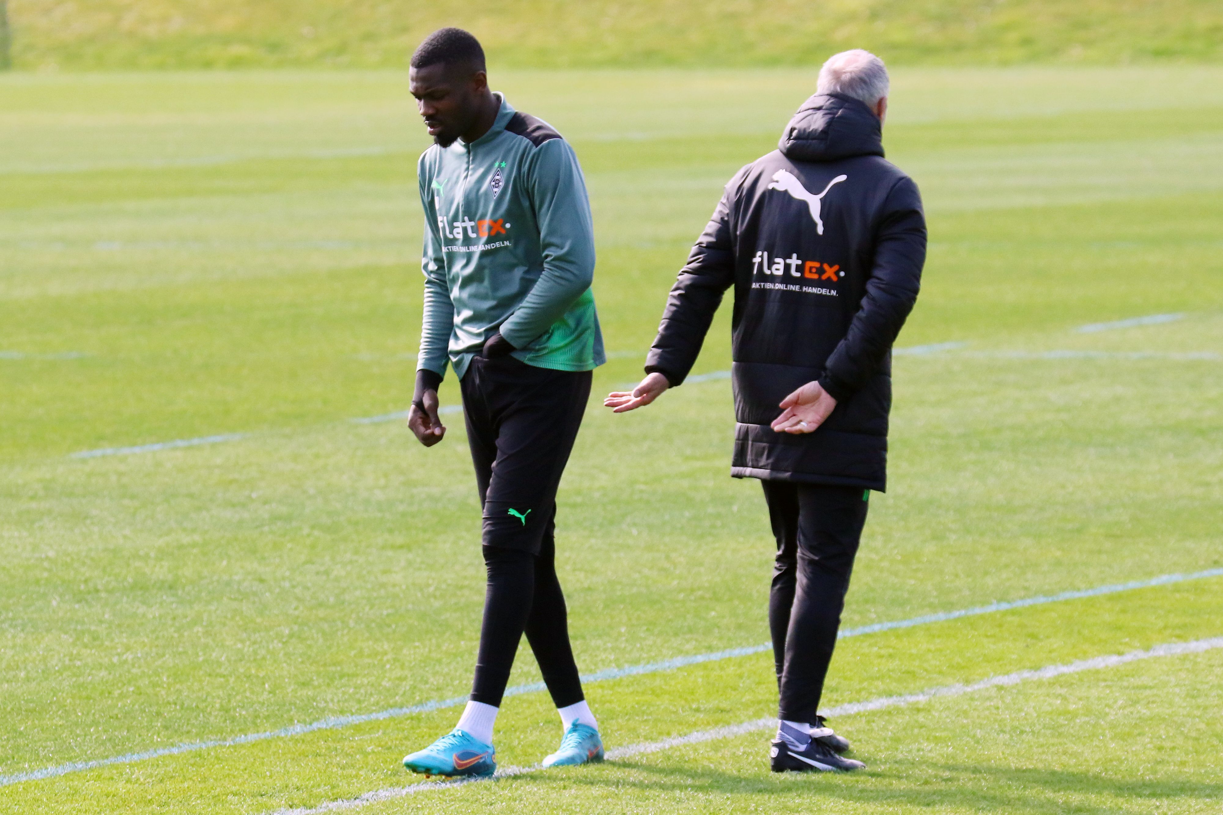 Marcus Thuram (l.) mit Coach Adi Hütter (r.) während einer Trainingseinheit im Borussia-Park am 30. März 2022. Thuram greift sich in die Hose.