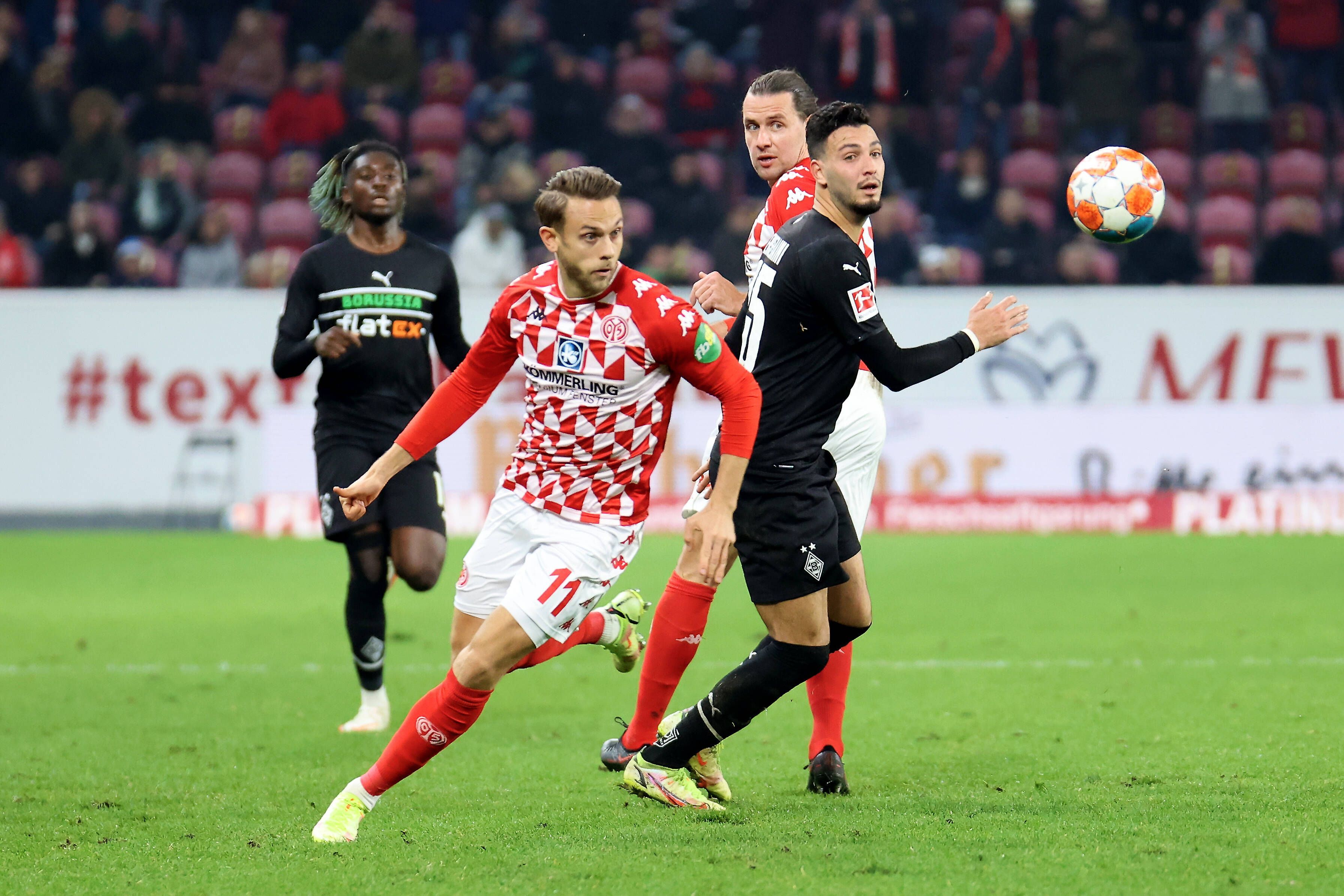 Ramy Bensebaini von Borussia Mönchengladbach (r.) im Duell mit Marcus Ingvartsen von Mainz 05 im Bundesliga-Hinspiel am 5. November 2021. Beide Spieler blicken auf den Fußball.