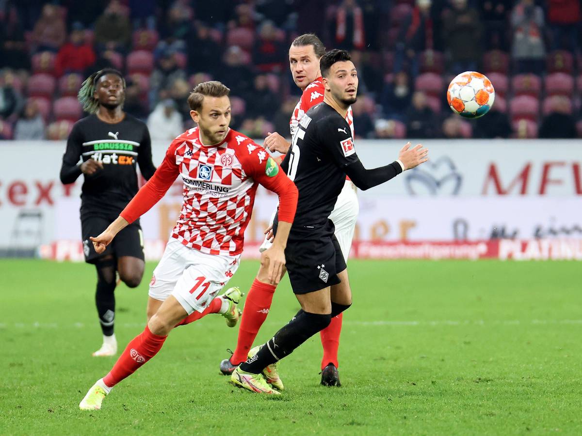 Ramy Bensebaini von Borussia Mönchengladbach (r.) im Duell mit Marcus Ingvartsen von Mainz 05 im Bundesliga-Hinspiel am 5. November 2021. Beide Spieler blicken auf den Fußball.