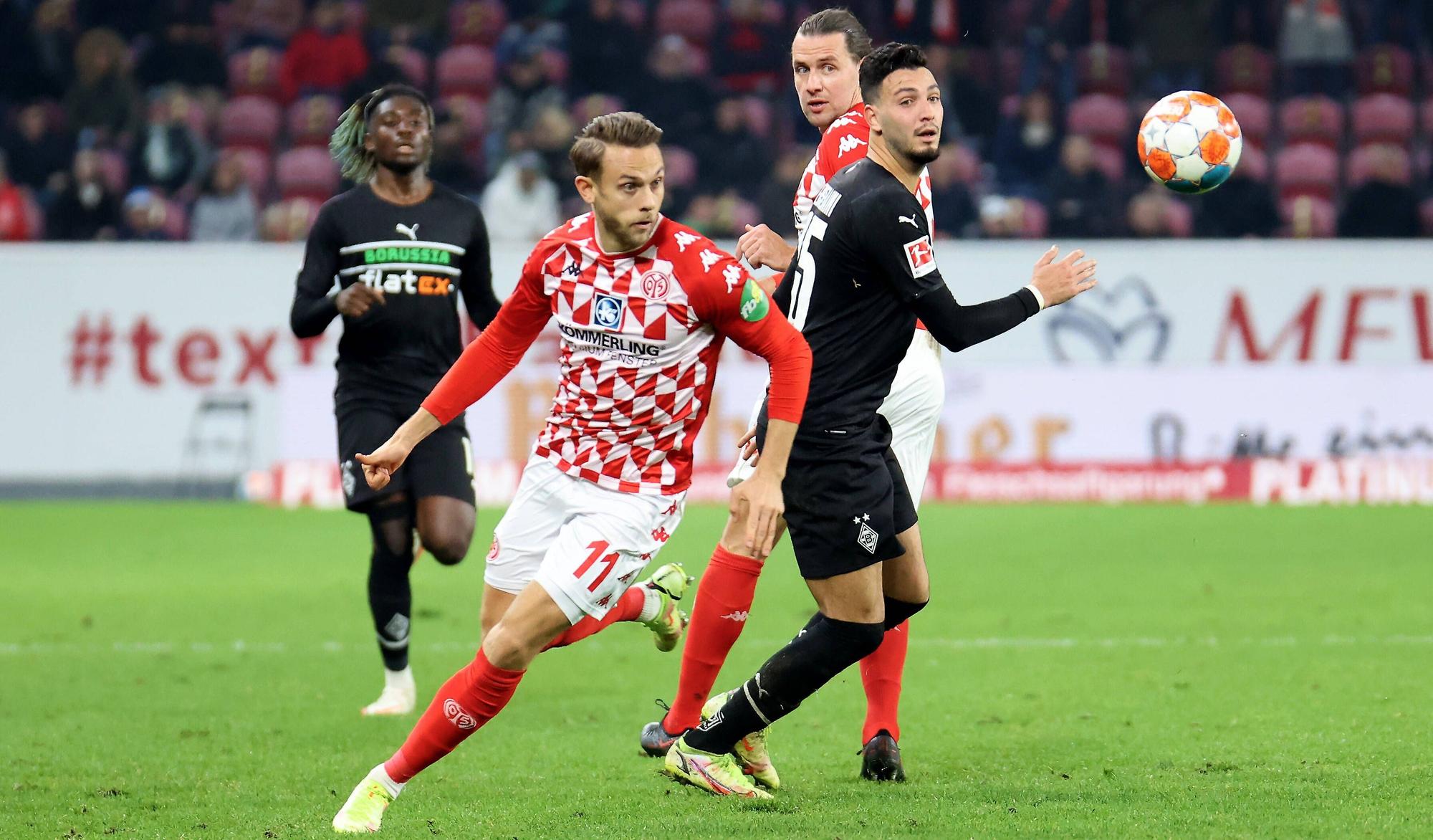 Ramy Bensebaini von Borussia Mönchengladbach (r.) im Duell mit Marcus Ingvartsen von Mainz 05 im Bundesliga-Hinspiel am 5. November 2021. Beide Spieler blicken auf den Fußball.
