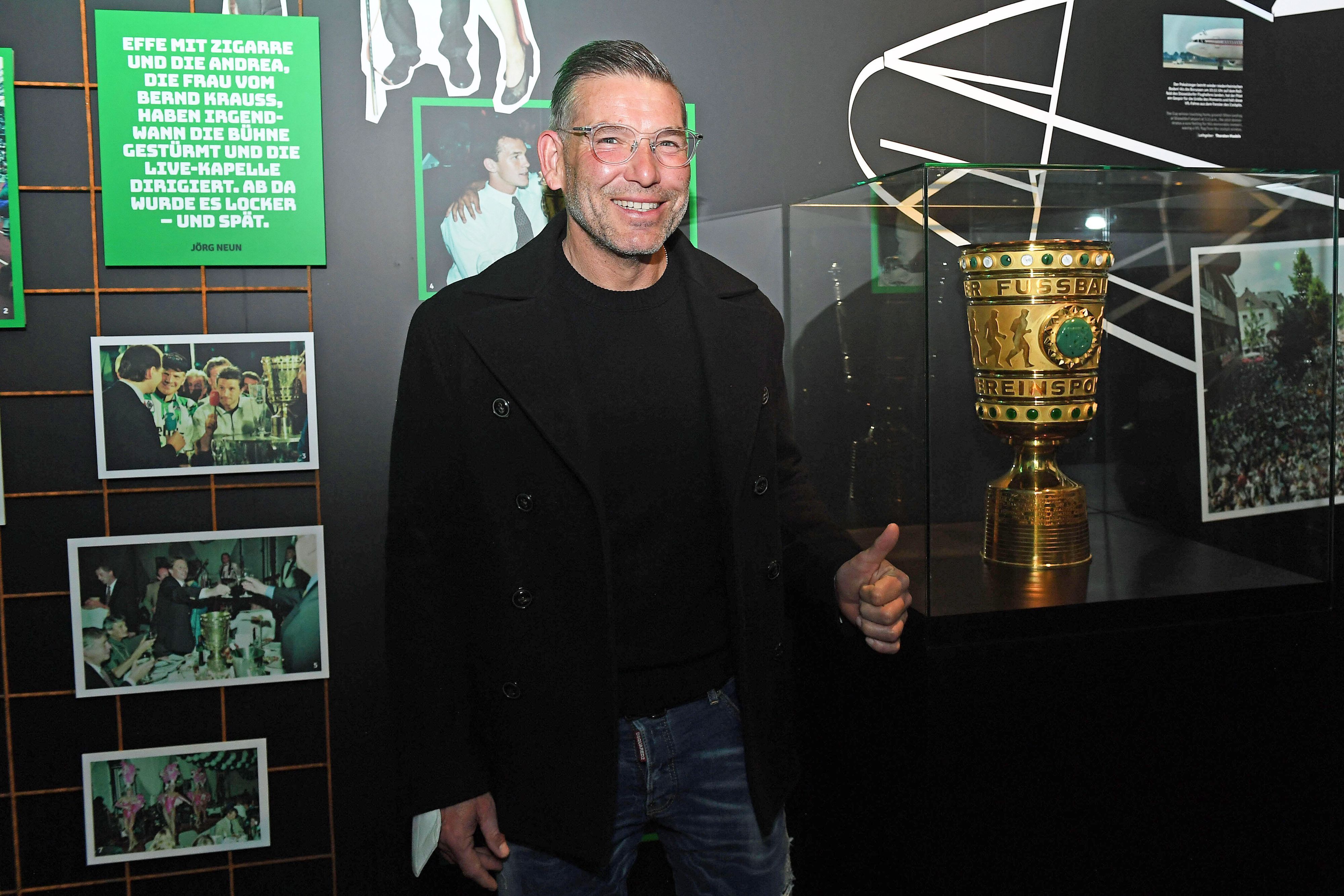 DFB-Pokalsieger und Torhüterlegende von Borussia Mönchengladbach, Uwe Kamps, in der Fohlen-Welt am 3. April 2022. Uwe Kamps steht lächelnd, mit dem linken Daumen nach oben, vor dem DFB-Pokal.