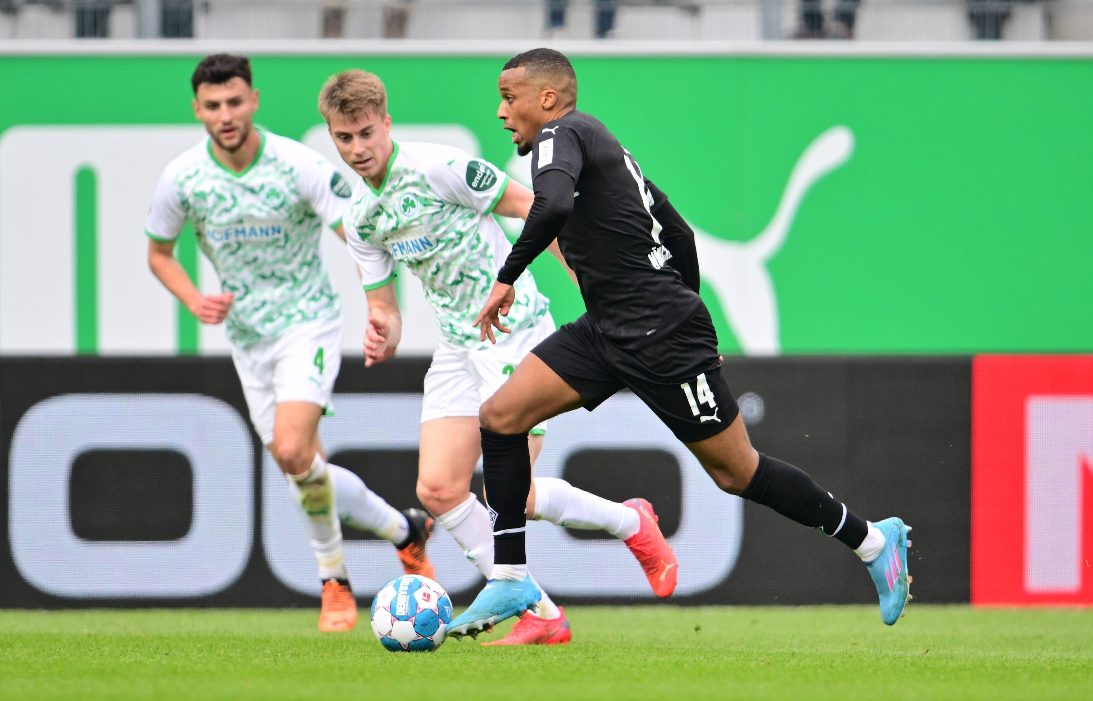 Gladbach-Stürmer Alassane Plea (r.) kann sich in dieser Szene gegen zwei Fürther Spieler durchsetzen (9. April 2022). Plea hat den Ball am Fuß.