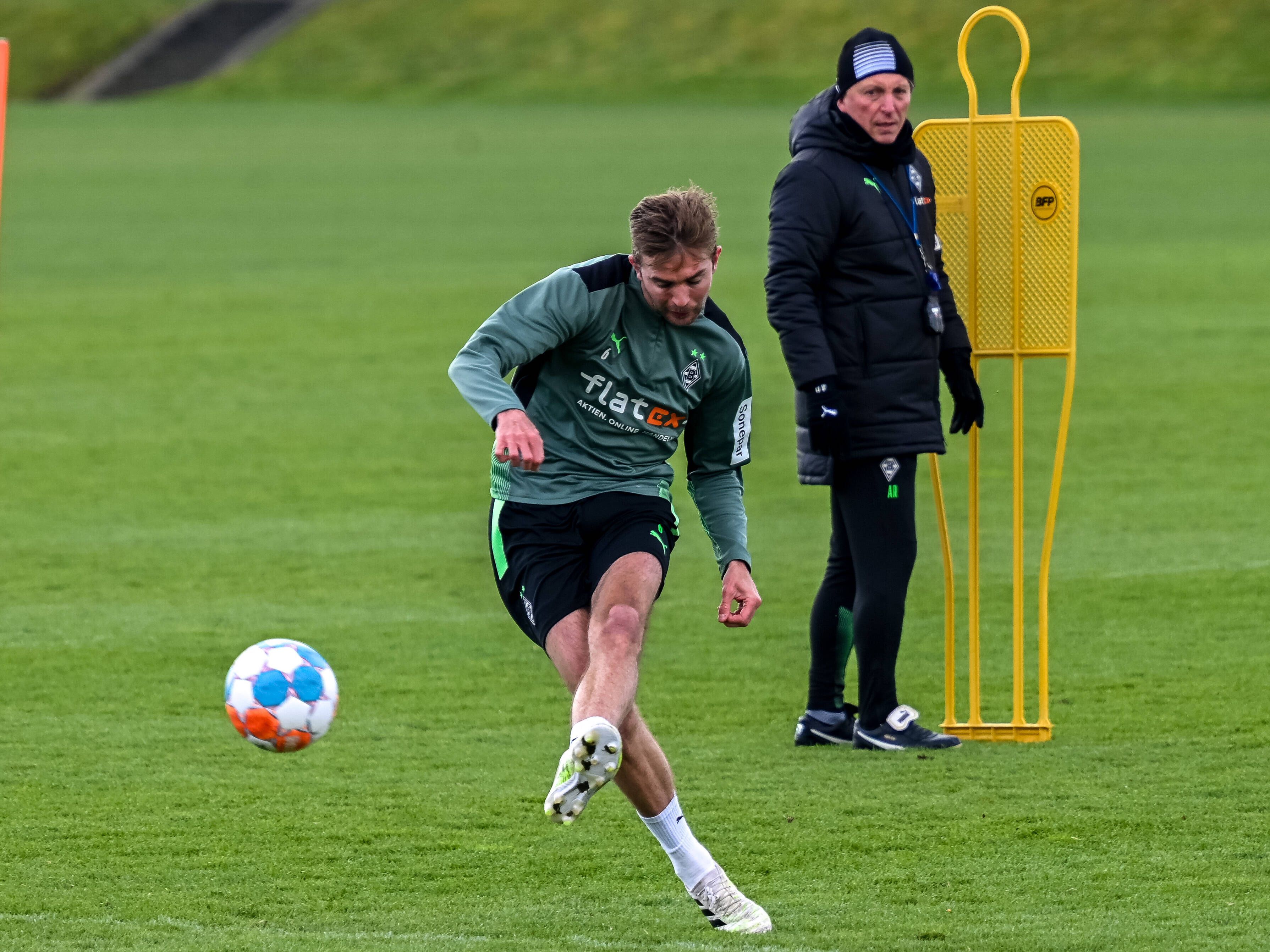 Gladbach-Profi Christoph Kramer am 10. April 2022 beim Torschusstraining im Borussia-Park. Im Hintergrund schaut Co-Trainer Armin Reutershahn zu. Kramer schießt den Ball.