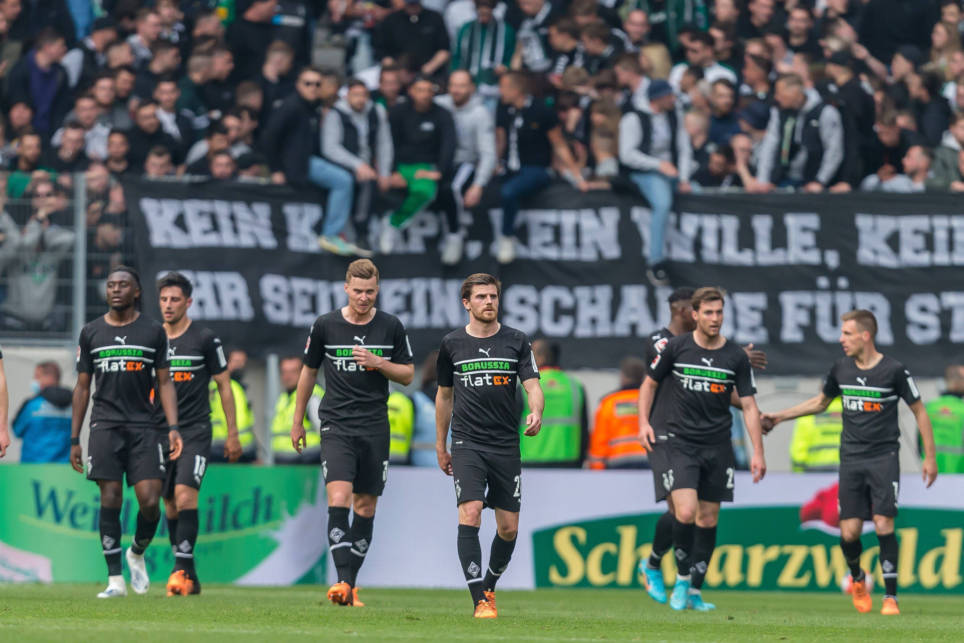 Die Spieler von Borussia Mönchengladbach schreiten nach dem 3:3 in Freiburg (23. April 2022) vom Rasen, im Hintergrund sind die Fohlen-Fans zu sehen. Am Zaun hängt ein Banner.