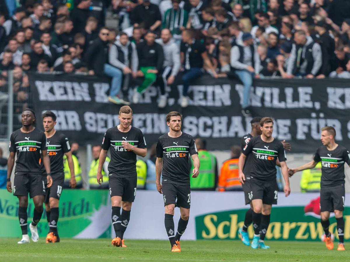 Die Spieler von Borussia Mönchengladbach schreiten nach dem 3:3 in Freiburg (23. April 2022) vom Rasen, im Hintergrund sind die Fohlen-Fans zu sehen. Am Zaun hängt ein Banner.