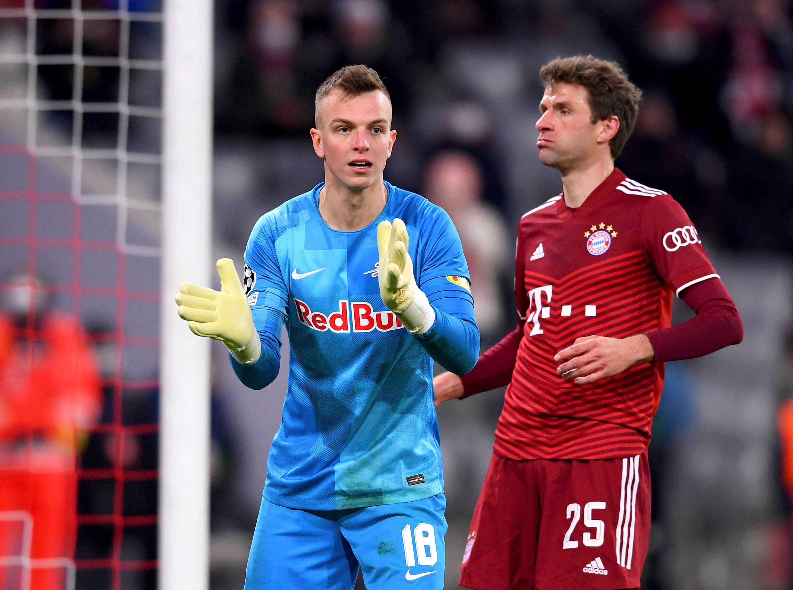 Torhüter Philipp Köhn von RB Salzburg (l.), hier zu sehen mit Bayern-München-Star Thomas Müller, während eines Champions-League-Spiels am 8. März 2022 in der Münchner Allianz-Arena. Köhn klatscht in die Hände.