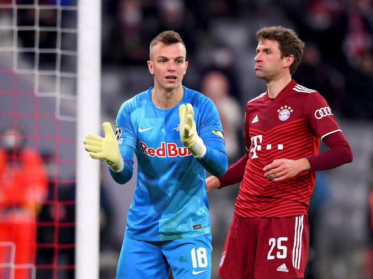 Torhüter Philipp Köhn von RB Salzburg (l.), hier zu sehen mit Bayern-München-Star Thomas Müller, während eines Champions-League-Spiels am 8. März 2022 in der Münchner Allianz-Arena. Köhn klatscht in die Hände.