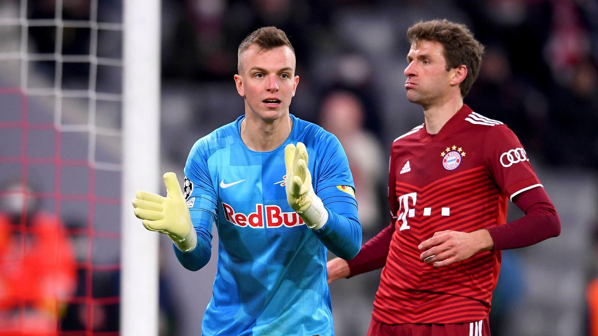 Torhüter Philipp Köhn von RB Salzburg (l.), hier zu sehen mit Bayern-München-Star Thomas Müller, während eines Champions-League-Spiels am 8. März 2022 in der Münchner Allianz-Arena. Köhn klatscht in die Hände.