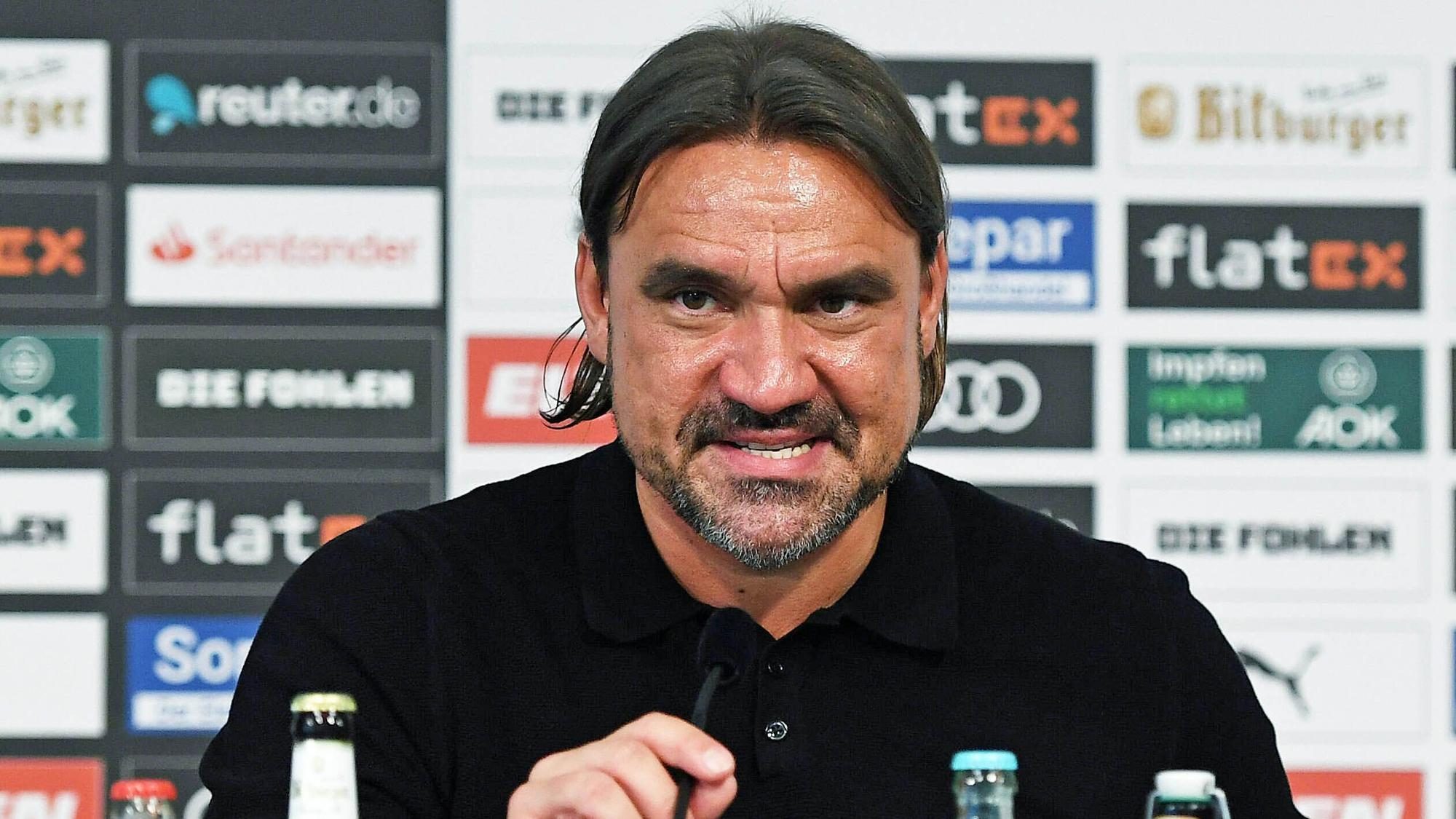 Daniel Farke, Trainer von Borussia Mönchengladbach, sitzt am 5. Juni 2022 im Presseraum im Borussia-Park vor einer Sponsorenwand. Farke trägt ein schwarzes Poloshirt. Mit seiner rechten Hand richtet er das Mikrofon.