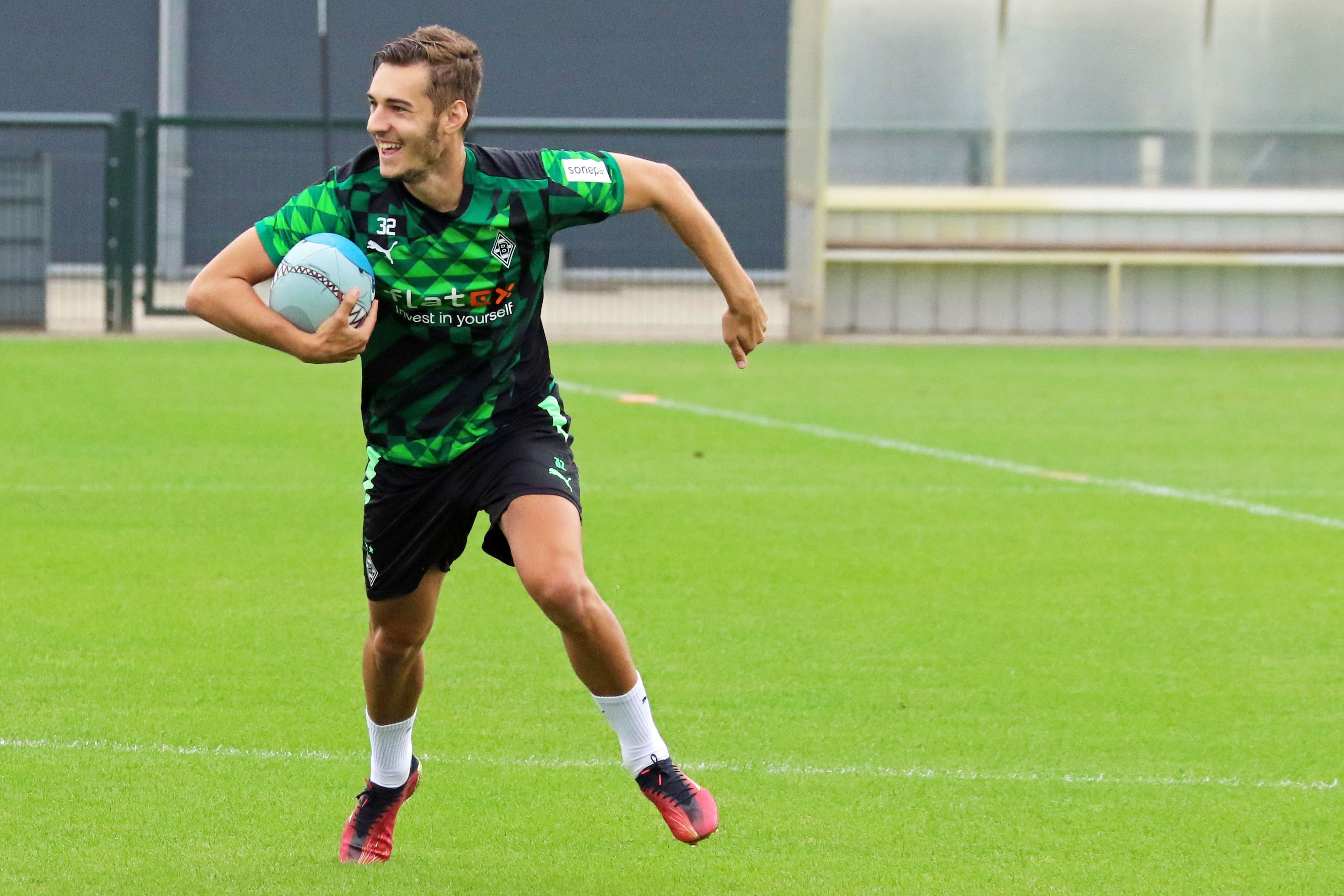 Gladbach-Profi Florian Neuhaus hat sichtlich Spaß beim Rugby. Dieses Foto stammt vom Training am 27. Juni 2022 im Borussia-Park. Neuhaus hält den Rugby-Ball fest und läuft.