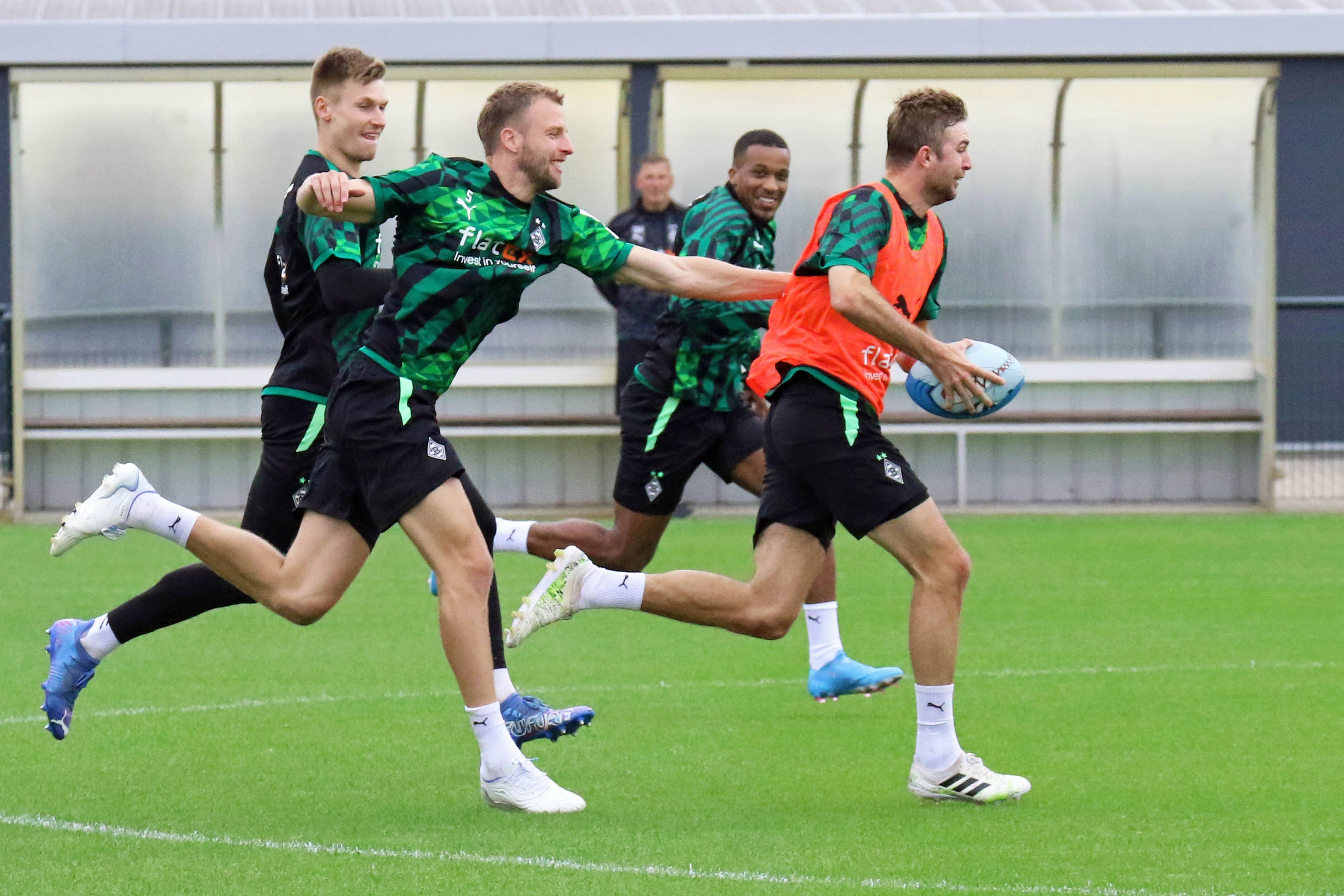 Weltmeister Christoph Kramer (r.) hat sich im Gladbach-Training (27. Juni 2022) das Rugby-Ei geschnappt und wird von Marvin Friedrich, Moritz Nicolas und Alassane Plea verfolgt. Kramer trägt ein orangenes Leibchen.