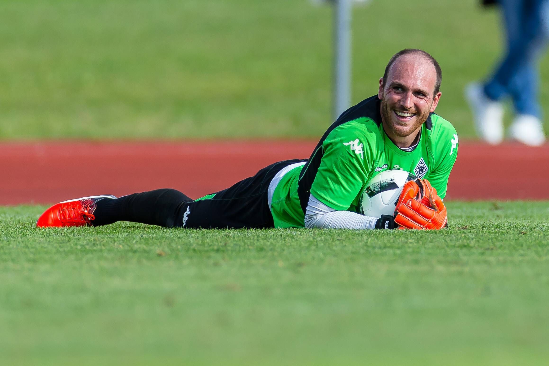 Gladbach-Keeper Tobias Sippel am 18. Juli 2016 im Trainingslager von Borussia Mönchengladbach in Rottach-Egern. Zu diesem Zeitpunkt sah die Frisur noch anders aus. Sippel liegt auf dem Rasen, hält einen Fußball fest und lacht.