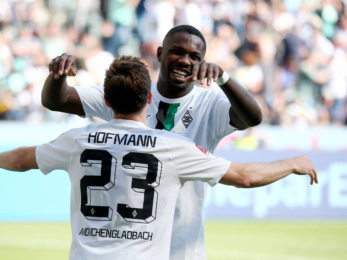 Die Gladbach-Profis Marcus Thuram und Jonas Hofmann jubeln in neuen Trikots beim Bundesliga-Heimsieg (5:1) gegen die TSG Hoffenheim (14. Mai 2022). Am ersten Spieltag der neuen Saison geht es für die Borussia erneut gegen Hoffenheim. Hofmann und Thuram (im Hintergrund) umarmen sich.