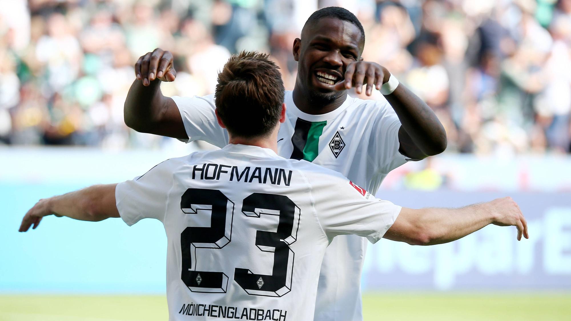 Die Gladbach-Profis Marcus Thuram und Jonas Hofmann jubeln in neuen Trikots beim Bundesliga-Heimsieg (5:1) gegen die TSG Hoffenheim (14. Mai 2022). Am ersten Spieltag der neuen Saison geht es für die Borussia erneut gegen Hoffenheim. Hofmann und Thuram (im Hintergrund) umarmen sich.