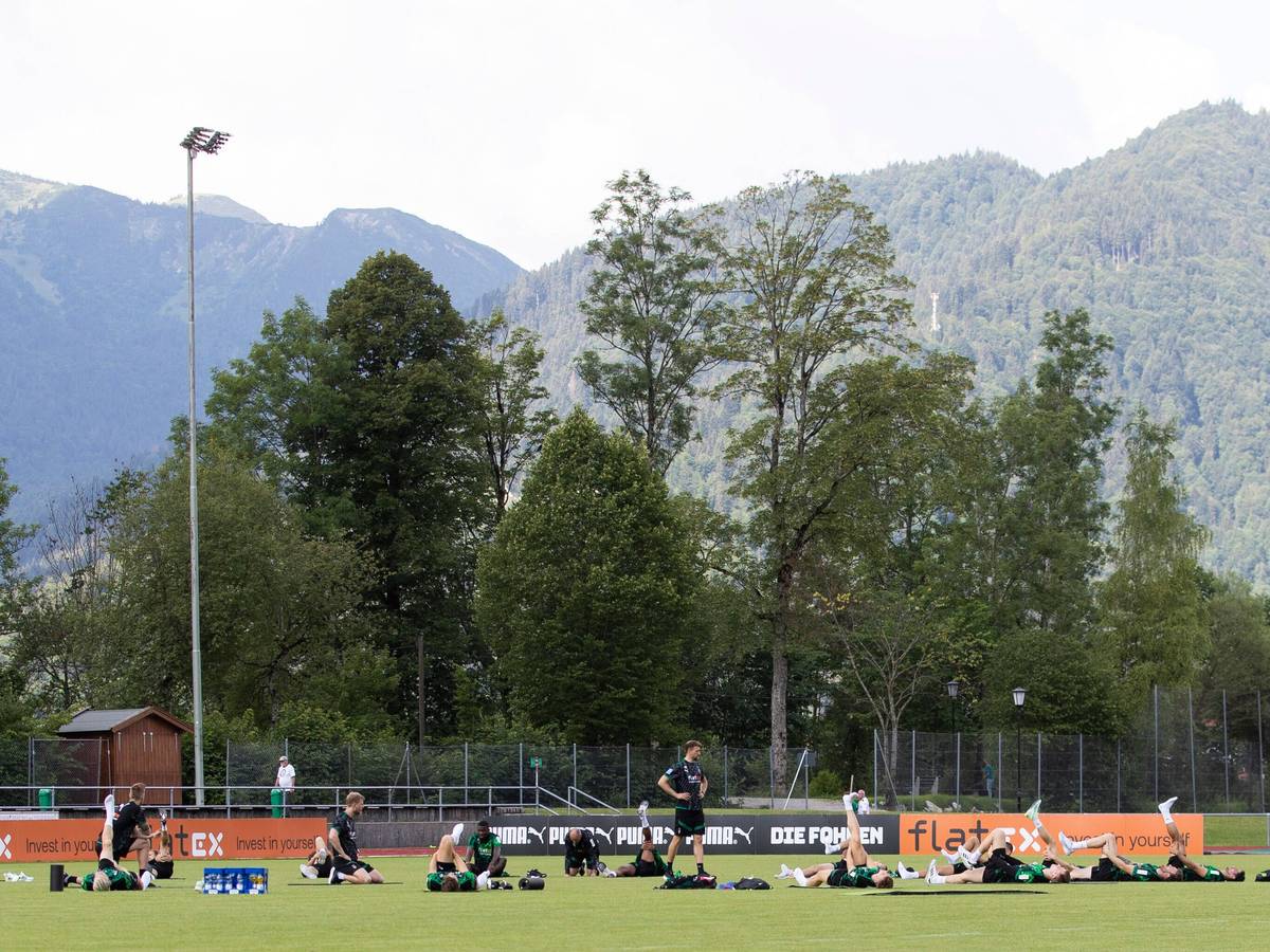 Die Gladbach-Profis im Trainingslager (6. Juli 2022) am Tegernsee in Rottach-Egern. Im Hintergrund sind die Bayerischen Alpen zu sehen. Die Spieler liegen auf dem Rasen und machen Stretching.