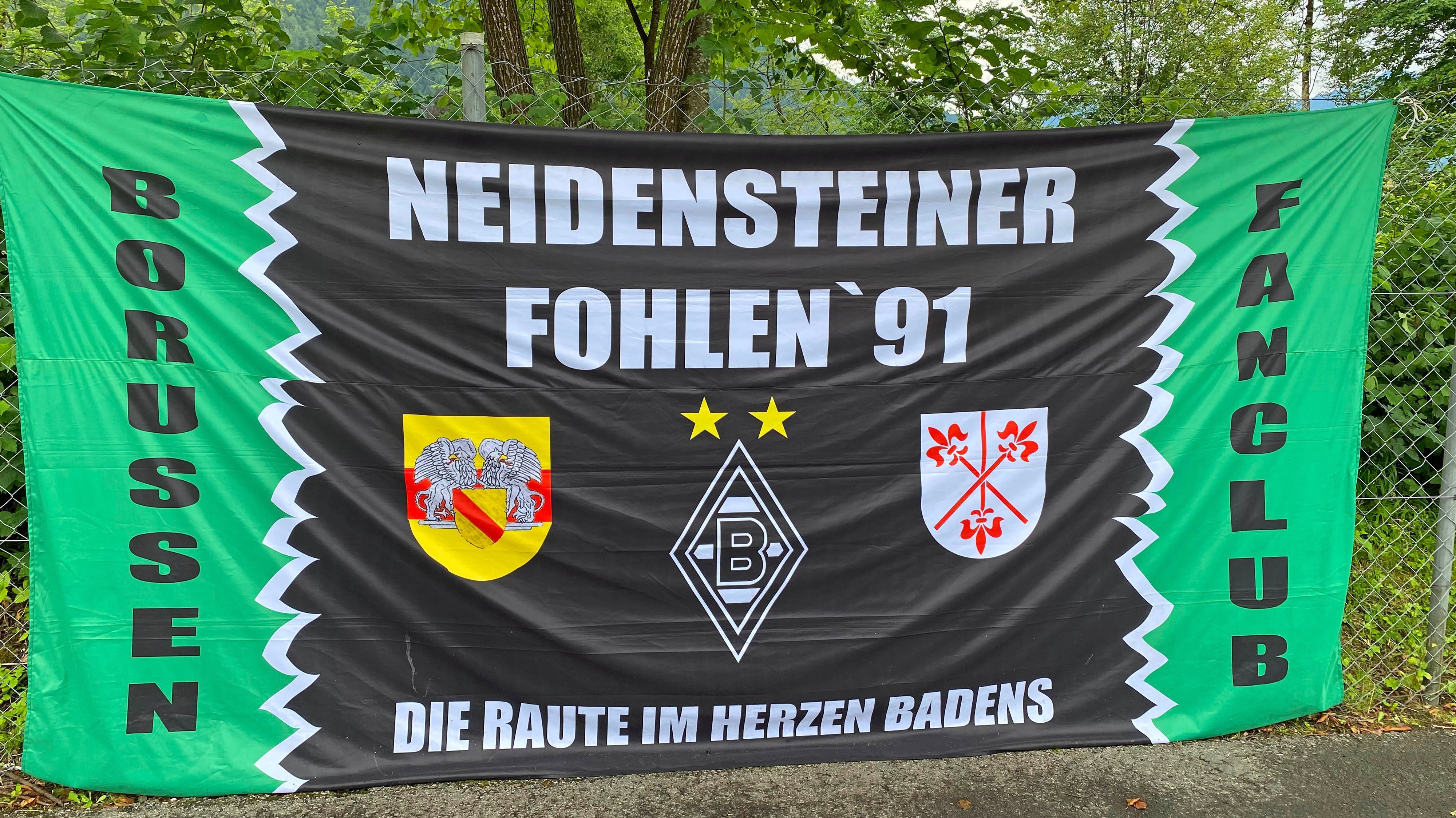 Das Banner des Gladbach-Fanklubs „Neidensteiner Fohlen '91“ ist auf der Sportanlage Birkenmoos in Rottach-Egern zu sehen. Die Fahne hängt an einem Zaun.