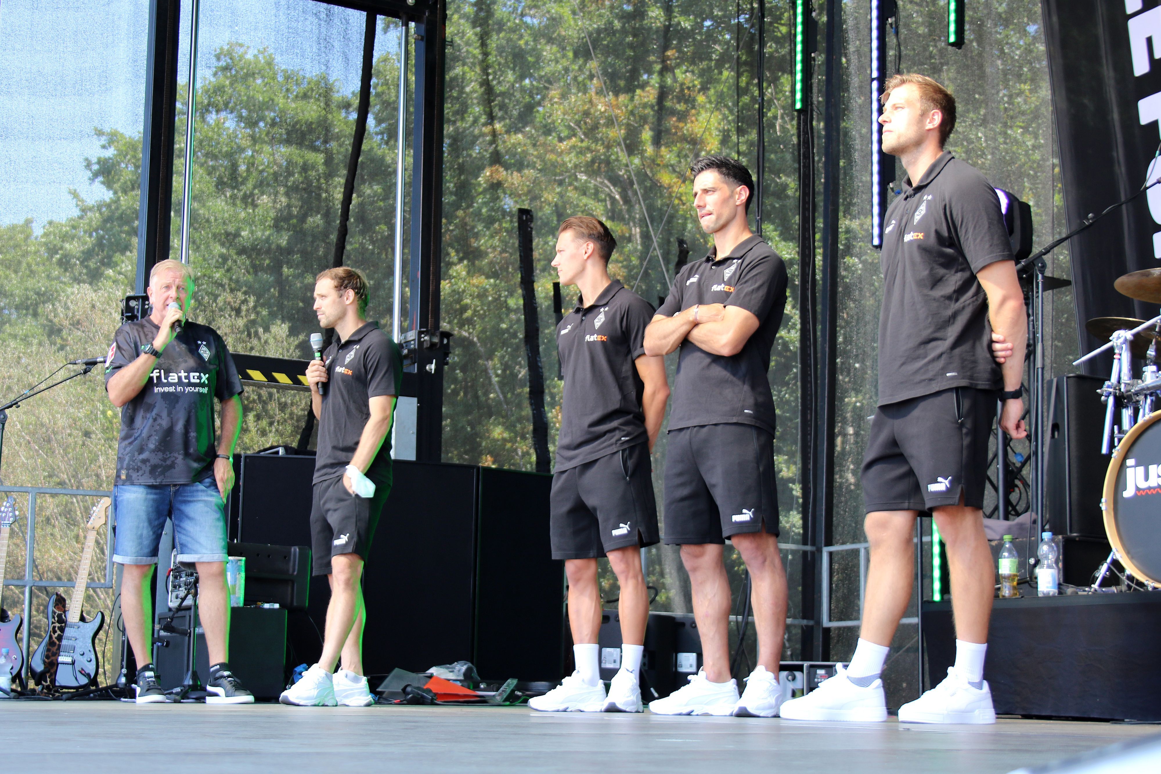 Moderator Frank Schiffers mit den Profis Tony Jantschke, Hannes Wolf, Lars Stindl und Torwarttrainer Fabian Otte (v.l.n.r) am 24. Juli 2022 bei der Saisoneröffnung von Borussia Mönchengladbach. Die Gruppe steht auf einer Bühne, Schiffers und Jantschke sprechen in ein Mikrofon.